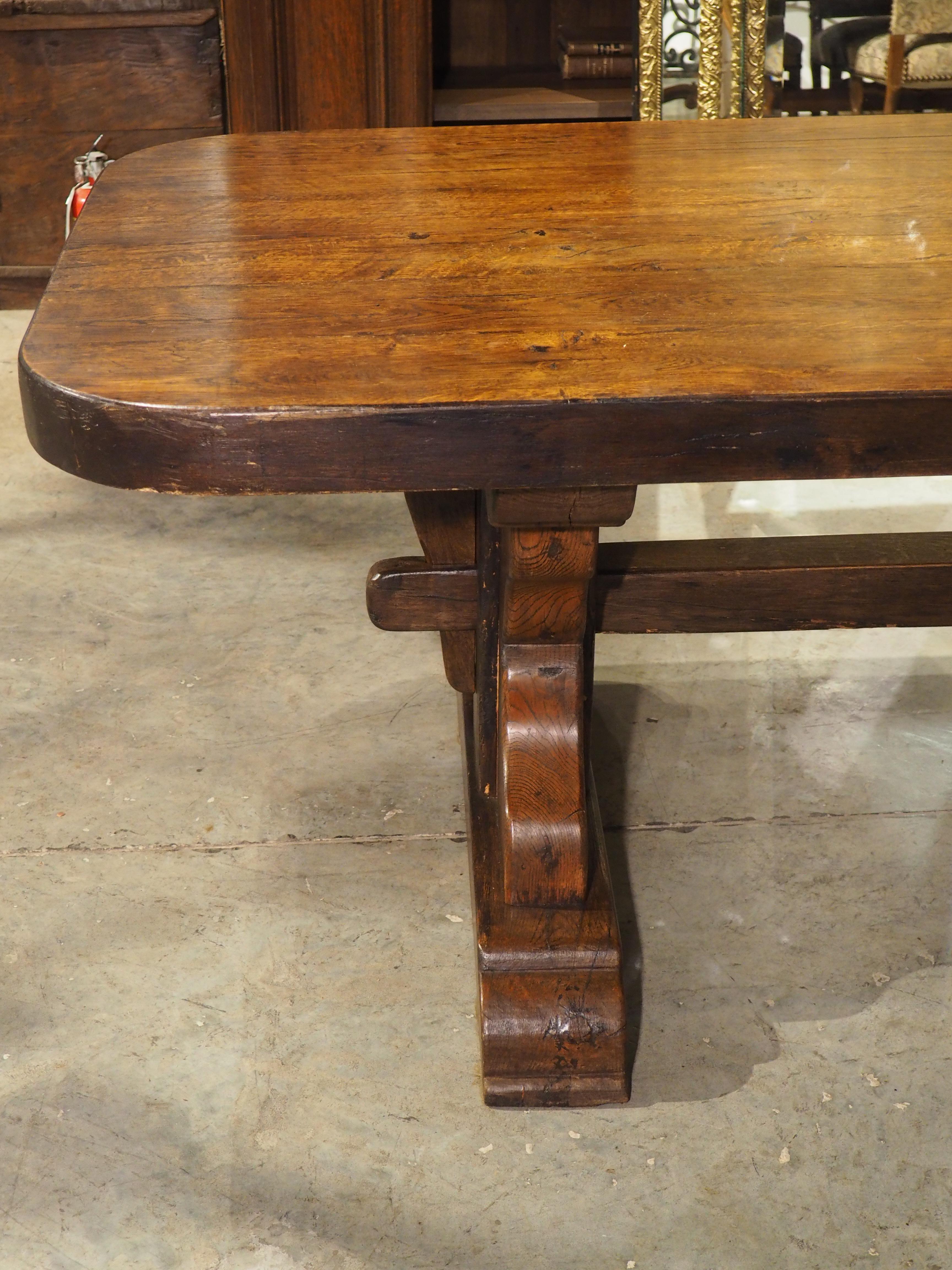 This fantastic large dining table with trestle supports and stretcher was produced in France, circa 1900. A three-inch-thick rectangular top, comprised of six oak planks, is supported by a pair of sinuously hand-carved legs. The center of each leg