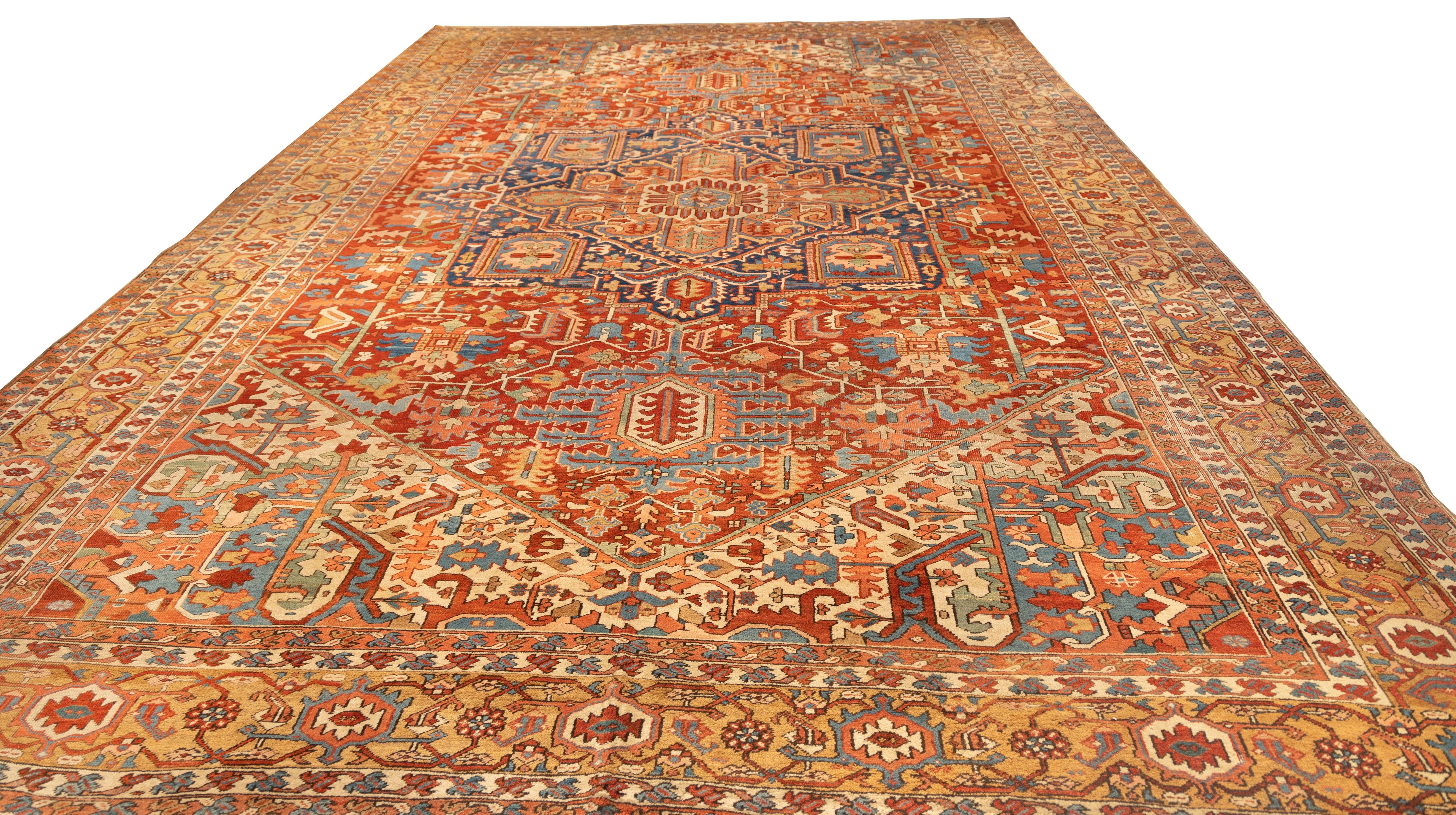 Oversized Early 20th century Heriz featuring a bold central medallion in deep navy, set against a vibrant rust-red field. Angular floral motifs, stylized rosettes, and stepped medallion corners are framed by intricate ivory spandrels and a