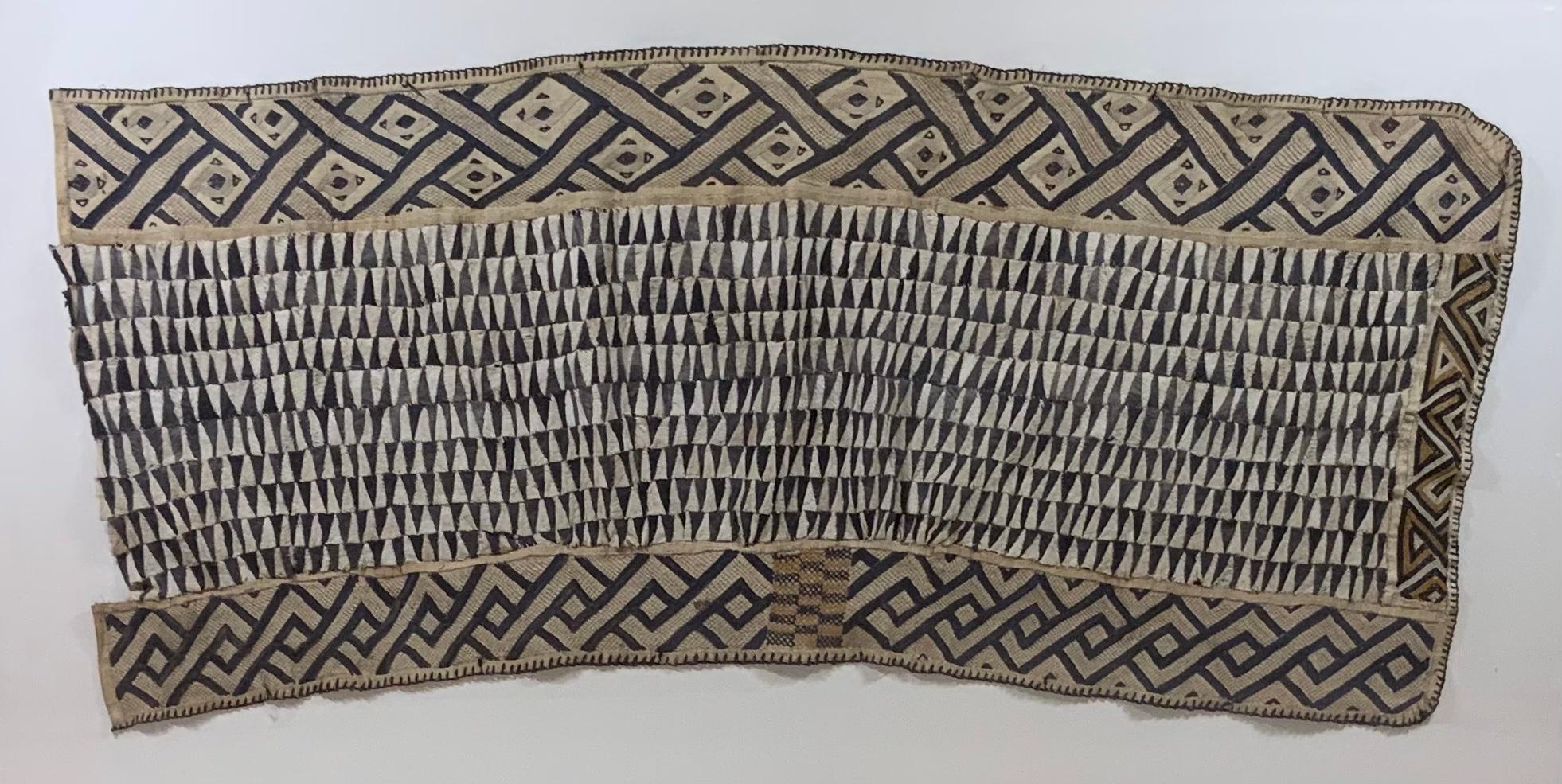 Professionally museum mounted exceptional antique African textile with brown small textile fragments woven into the geometric pattern in raffia and cotton patchwork , interlock border appliqué panel around three sides of the textile .
Great