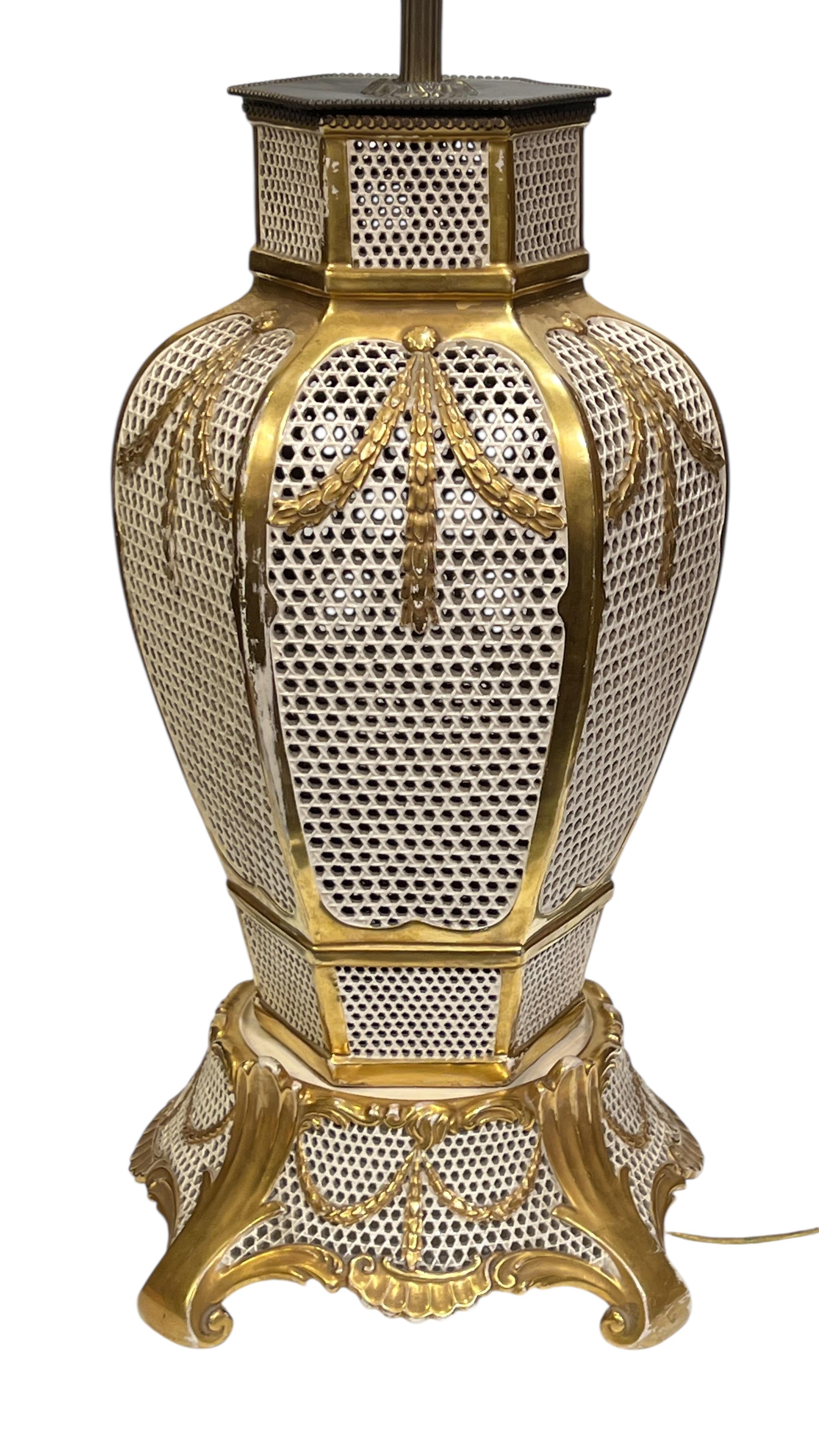Antique (early 20th century) table lamp by Fischer of Budapest Hungary with hexagonal vase shape set upon four scrolling legs, distinguished by its size and openwork design with partially gilt white glazed finish.  30 inches tall to the top of the