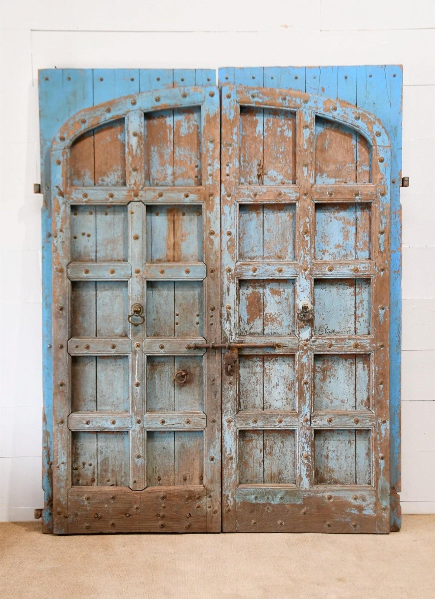 A magnificent pair of historic antique Indian hand carved and painted solid wood entry doors. 

The monumental castle size, strong forged iron mounted, heavily reinforced solid teak construction indicate they were likely originally used to keep a