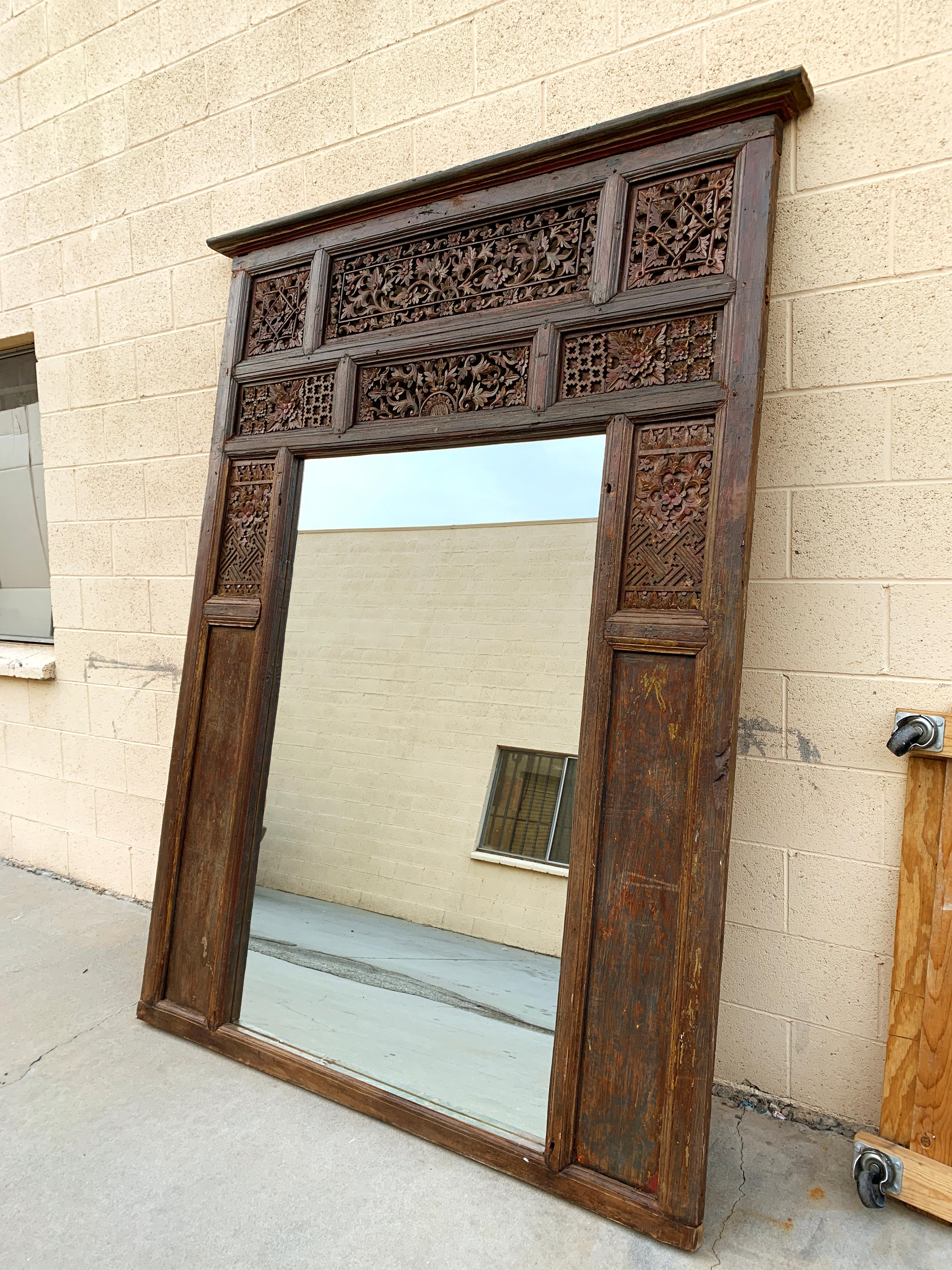 This impressive mirror was repurposed from an old window frame from the Rajasthan region of India. The teak wood features a beautiful carved floral motif. Unique patina shows wonderful variations in color. One-of-a-kind. 

Dimensions: 92