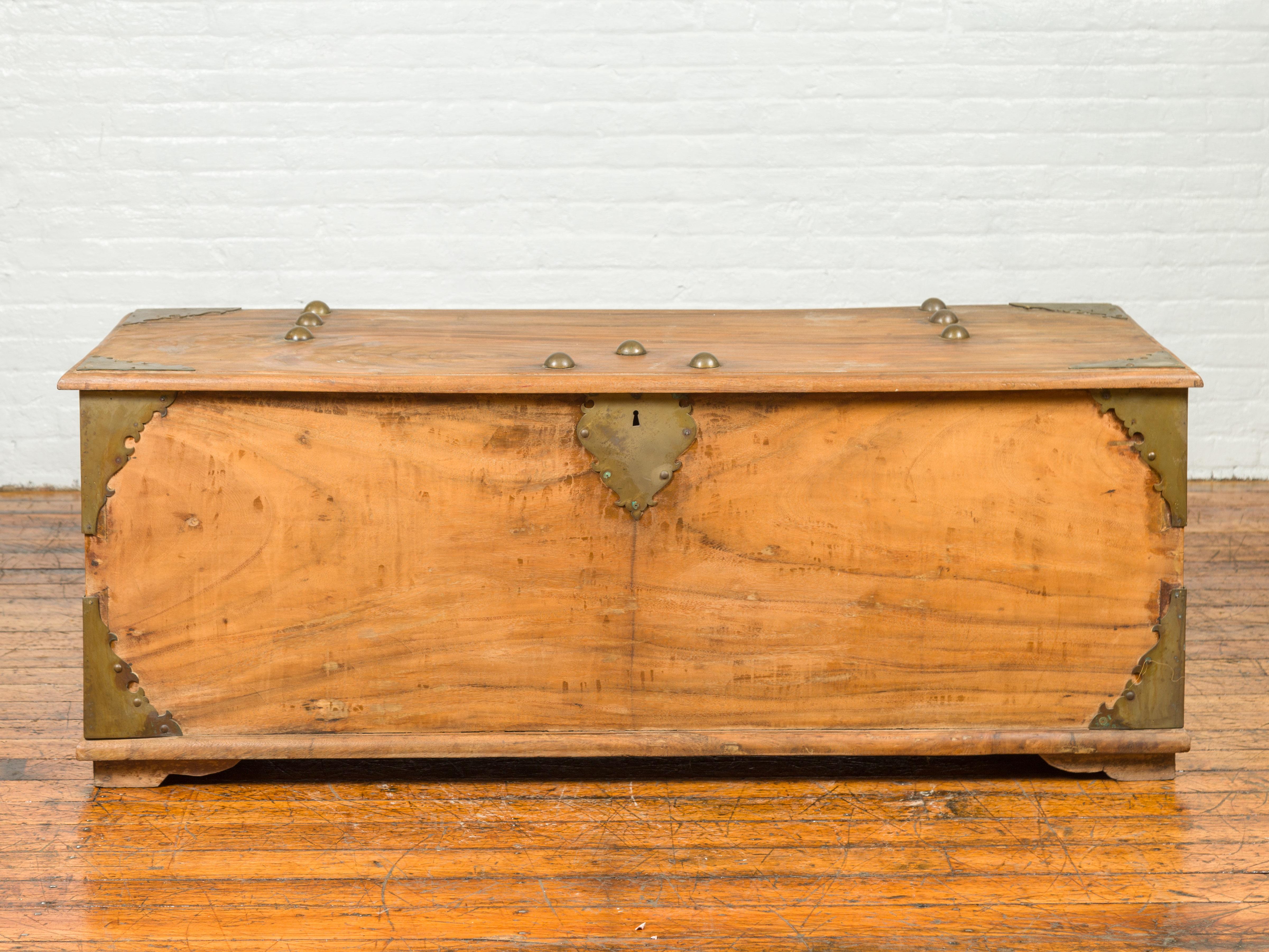 A large Indian antique wooden blanket chest from the 19th century with bronze hardware and round dowels. Attracting our attention with its large proportions, this antique blanket chest features a rectangular lid with bronze accents and round dowels,