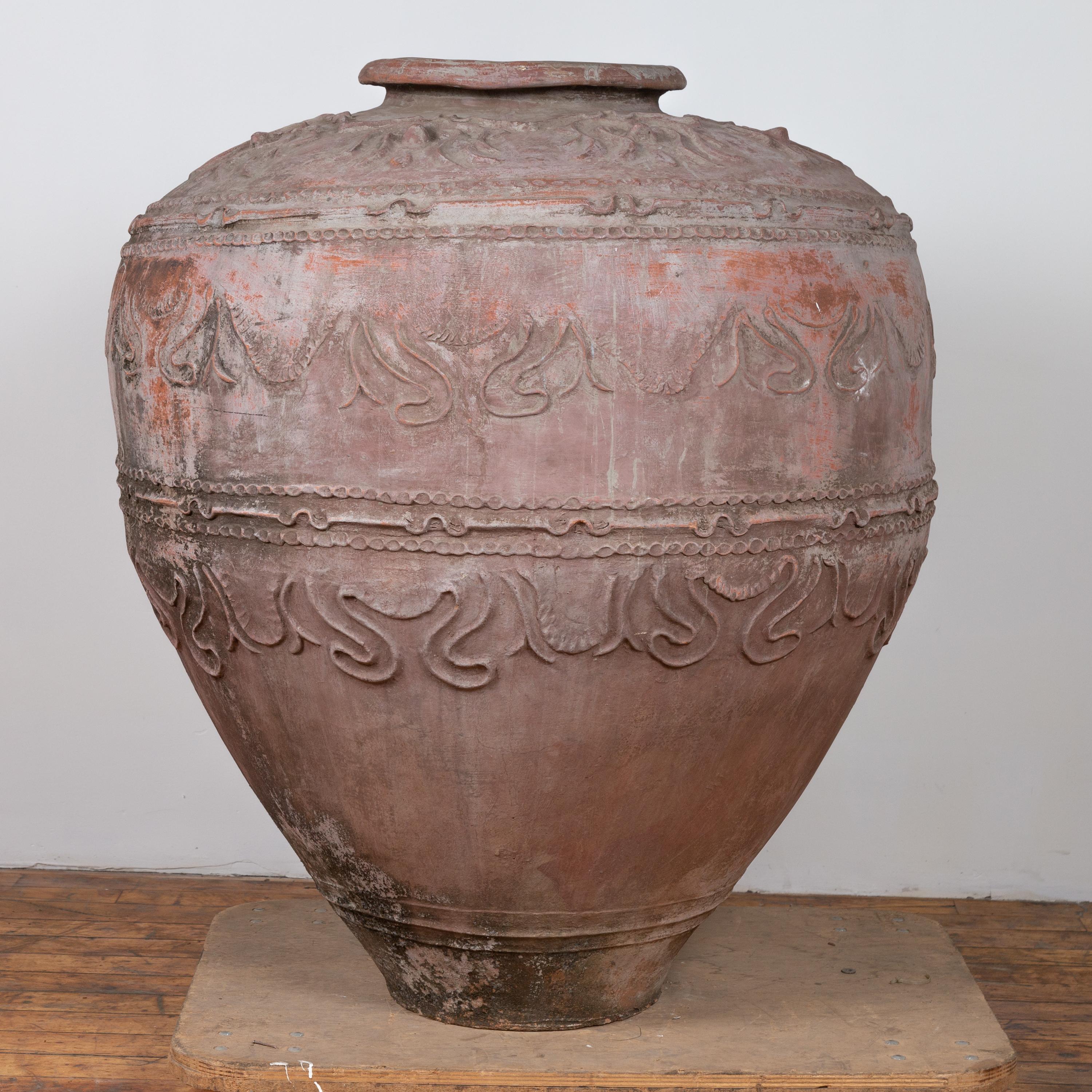 A large antique Indonesian terracotta water jar with wavy patterns, hollow beaded motifs and nicely weathered appearance. Born in Indonesia, this terracotta jar attracts our attention with its large proportions and aged patina. Presenting a thin lip