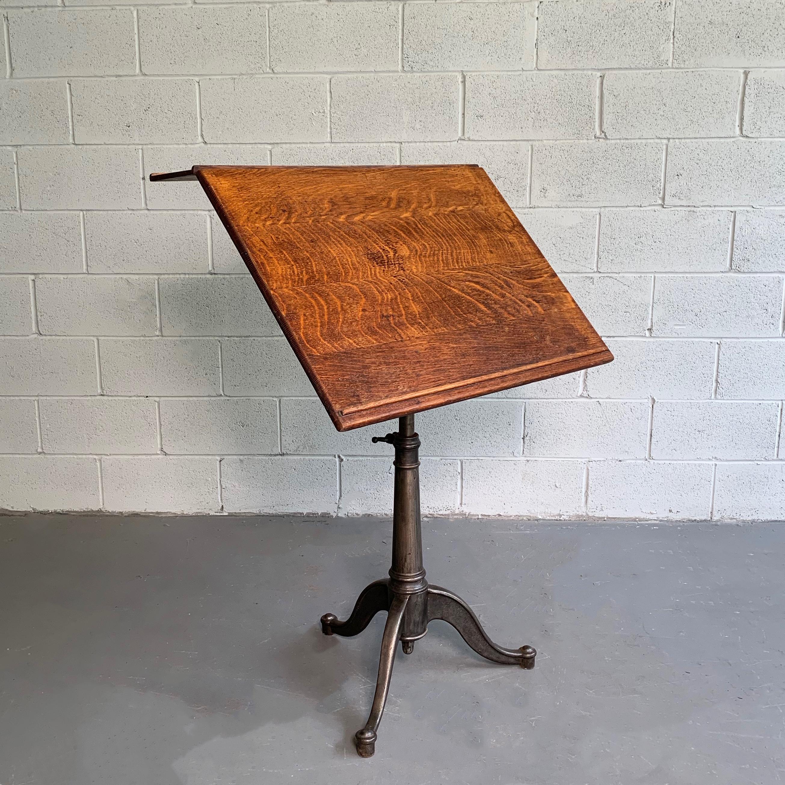 Large, antique, industrial, artist rendering easel table features an expandable, oak top from 22.5-29 inches with a 6.5 inch lip on a tilt and height adjustable cast iron pedestal base that adjusts from 29-40 inches height.