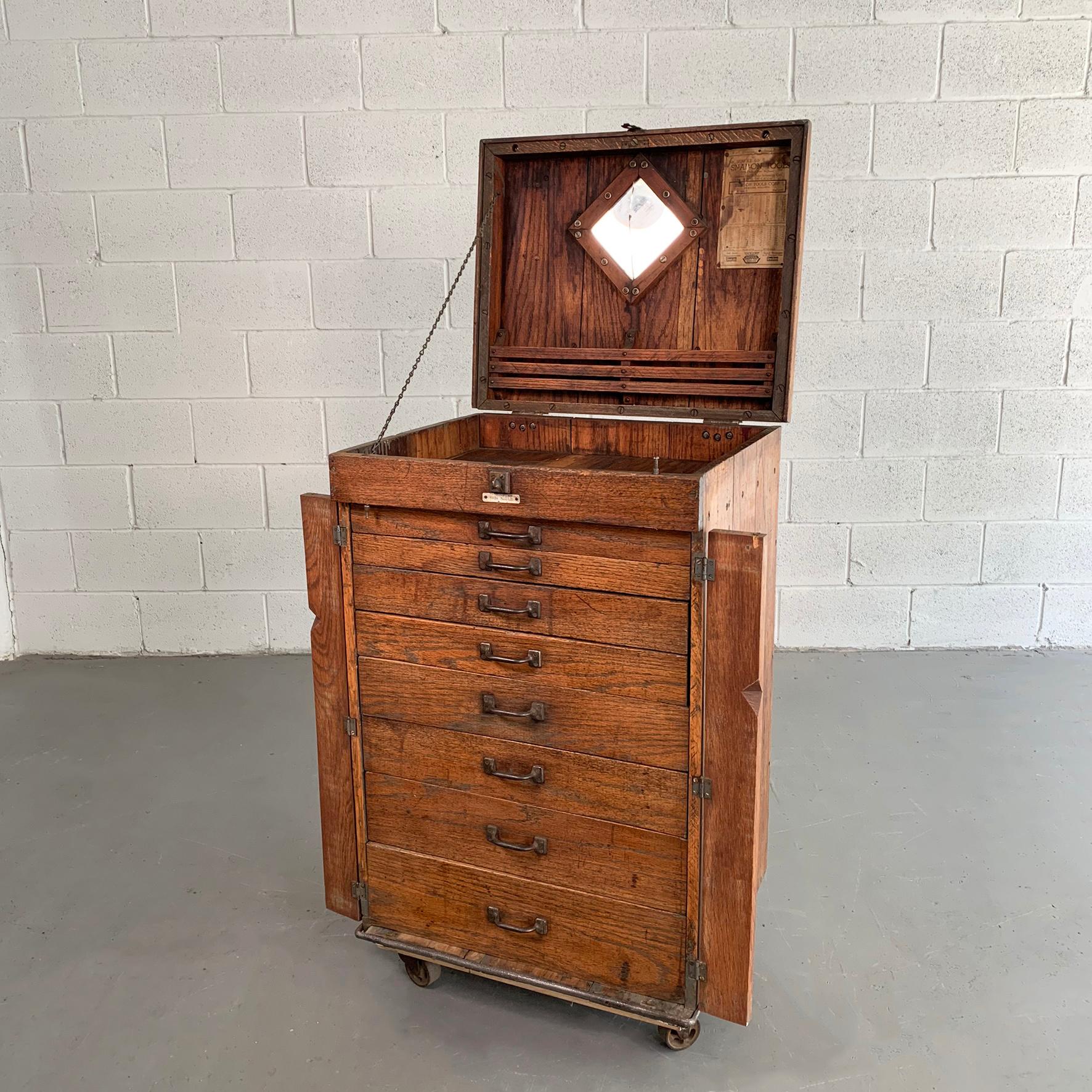 Large, antique, industrial, turn of the century, oak, machinist tool chest cabinet features several divided drawers with cast metal hardware that can be locked with a padlock when closed and rolls on casters. The Snap-On tool chart is a later