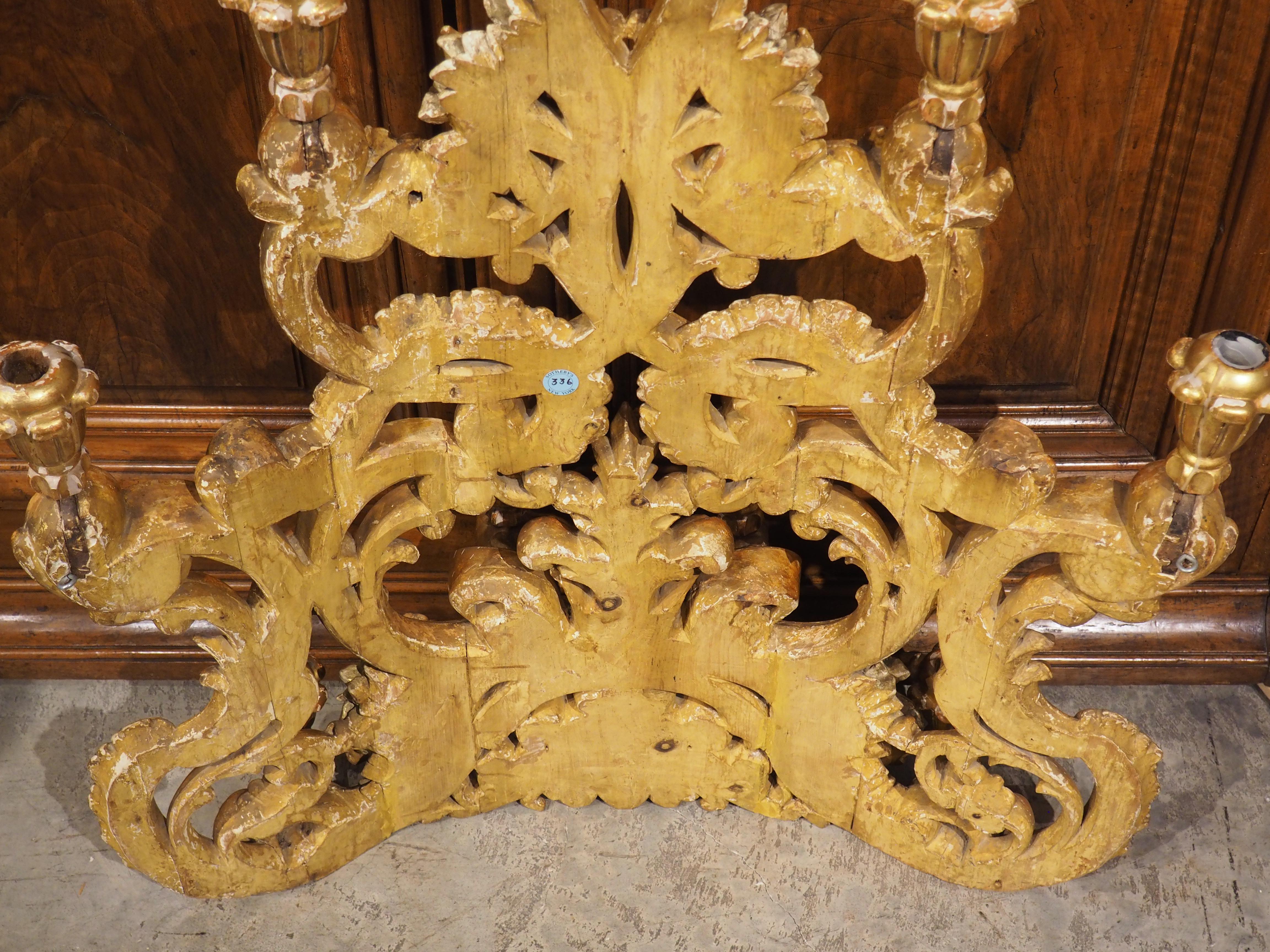A beautiful display of flowers and foliage adorn this large, wall hanging giltwood eight-light candelabra.  Hand-carved circa 1750 in Italy, the vegetation is accompanied by a twisting, vine-like arabesque. Additional motifs include attenuated