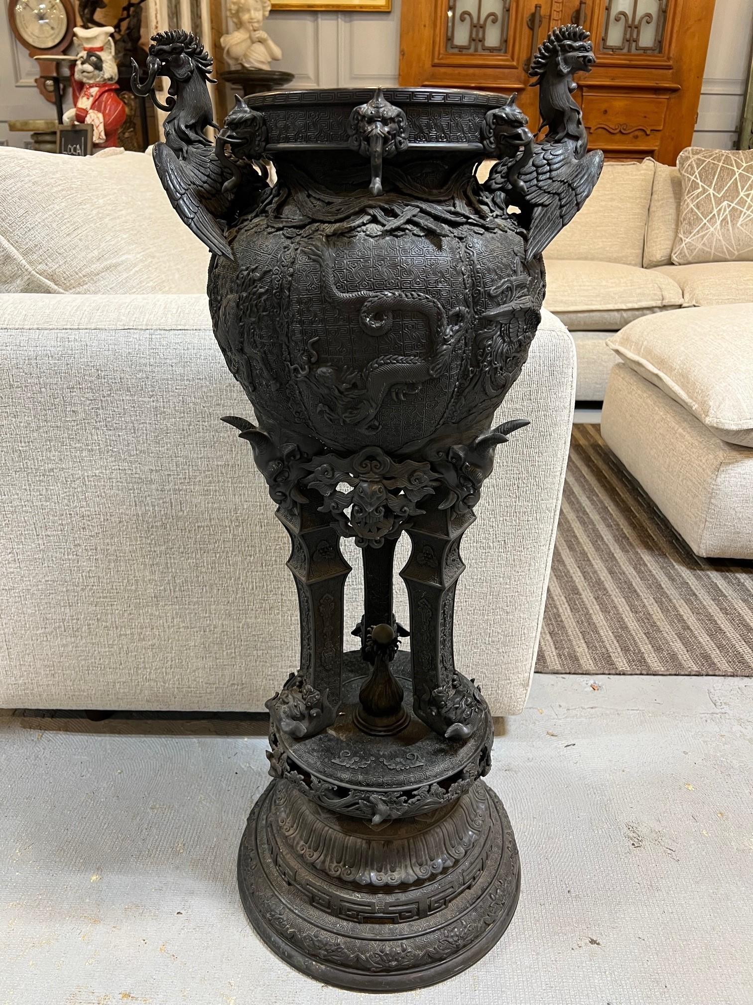 Dating from the Meiji period this standing Japanese Koro or incense burner has a circular stepped base. Three legs topped with horned and other demons standing on upside down foo dogs. Elephant heads on the rim and phoenix birds, wing spread, upper
