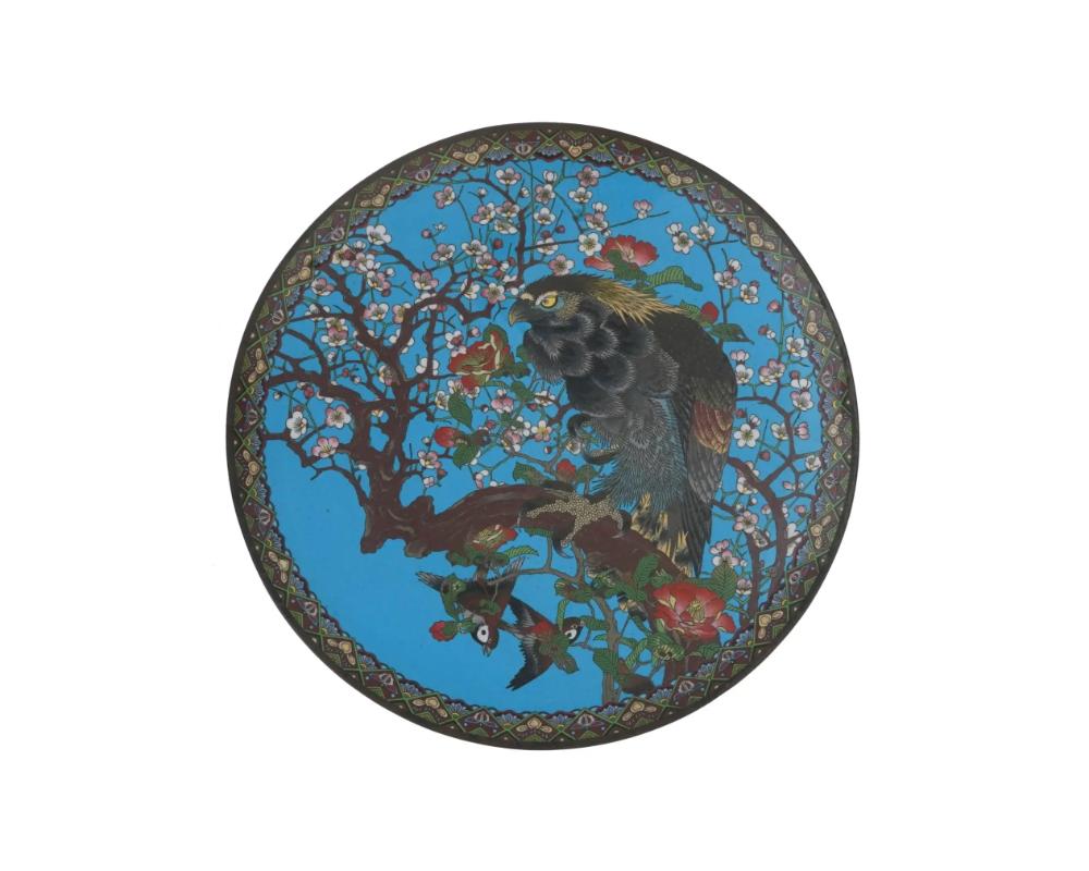 An antique Japanese late Meiji era decorative enamel over copper charger plate. The interior of the plate is adorned with a polychrome image of a hawk seated on a sakura tree branch, and a pair of birds in blossoming flowers made in the Cloisonne