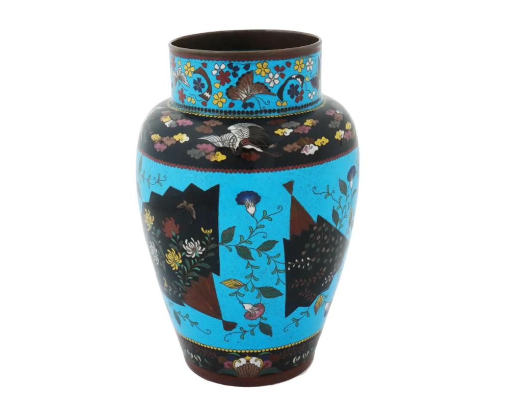 A large antique Japanese Meiji era enamel over copper vase. The urn shaped vase is enameled with polychrome fan shaped medallions featuring floral, foliage and butterfly motifs surrounded by floral and foliage patterns made in the Cloisonne