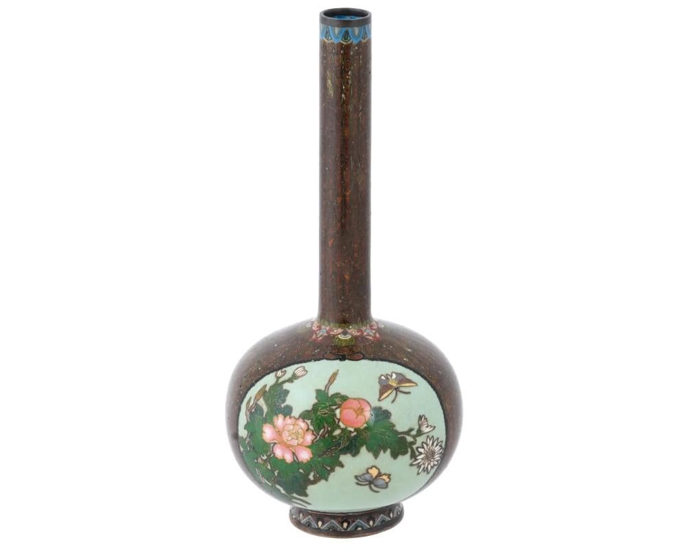 A large antique Japanese, Meiji era, enamel over copper vase. The vase has a globular shaped body and a long narrow neck. The ware is enameled with polychrome medallions depicting a bird and butterflies in blossoming flowers surrounded by a scaly