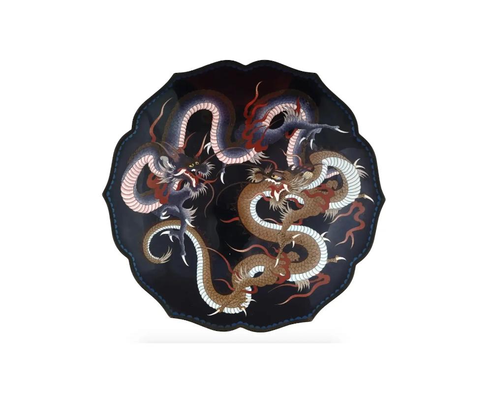 A large antique Japanese Meiji period cloisonne enamel charger. The central motif of this charger consists of two dragons, a common and powerful symbol in Asian culture. These dragons are depicted in a fierce and dynamic dueling posture, with
