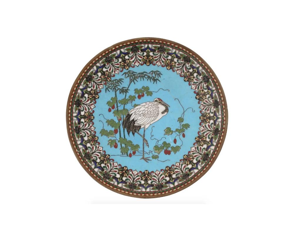 A large antique Japanese Meiji era enamel over brass charger plate. The plate is enameled with a polychrome image of a naturalistic crane in bamboo trees and branches on turquoise ground made in the Cloisonne technique. The border is decorated with