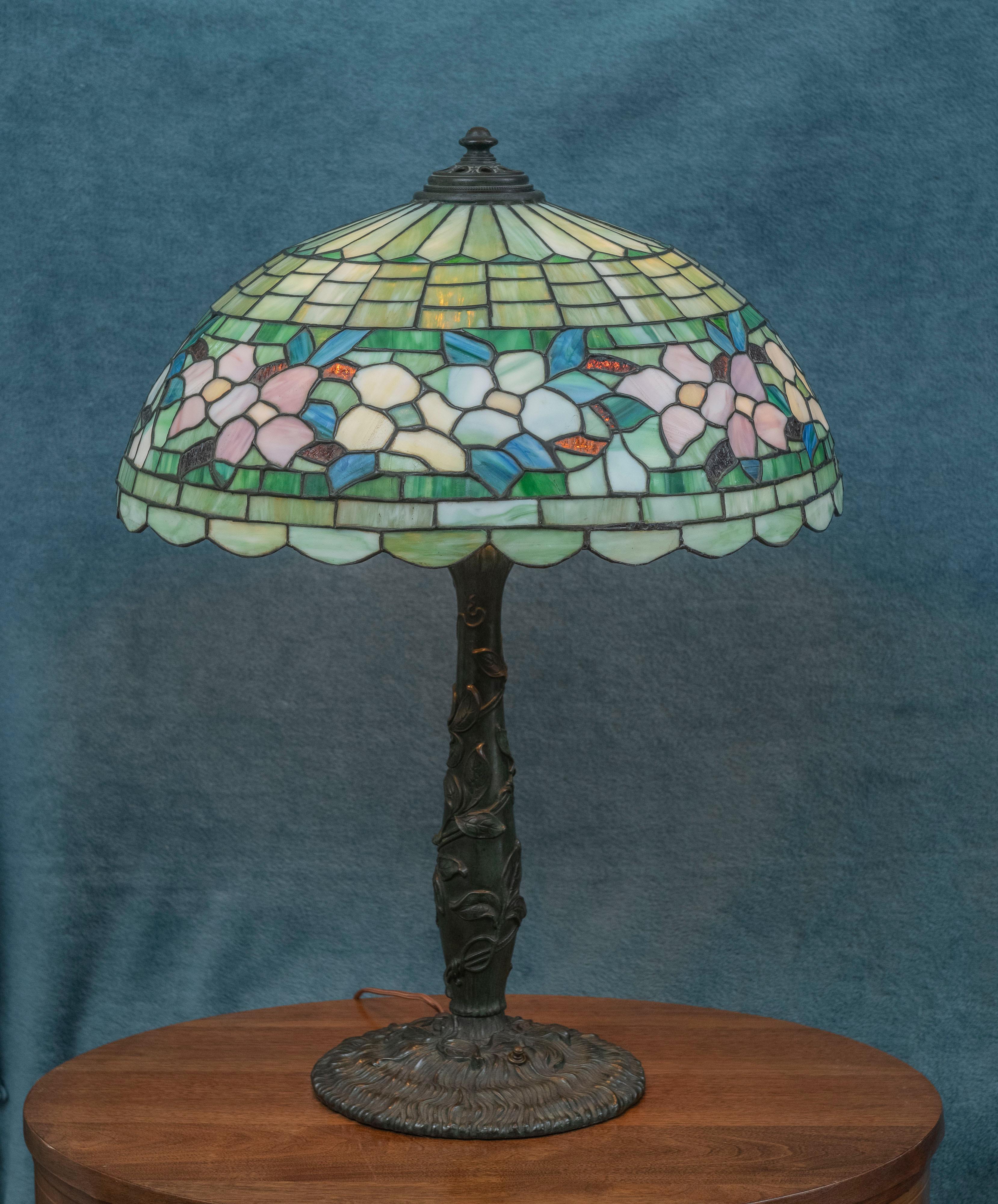  This high quality and colorful lamp by Wilkinson is a fine example of his workmanship. This dogwood floral border shade is pictured on the top of page 166 in the book Mosaic Shades Volume II, by Paul Crist. Our base is a different model as
