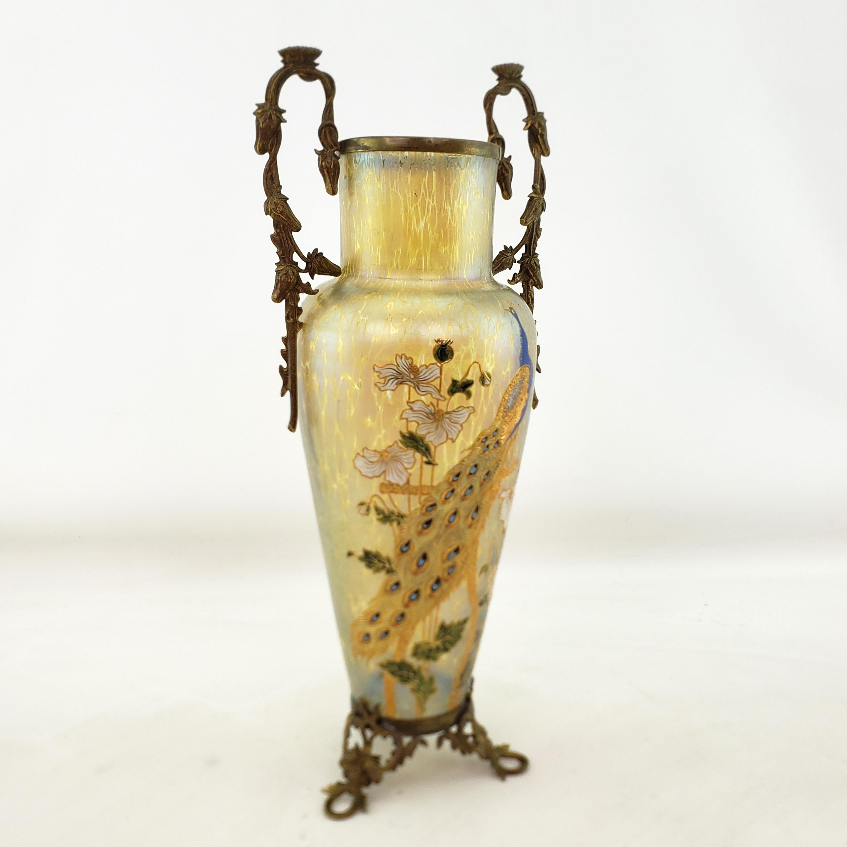 This antique vase is unsigned, but made by the Loetz glass factory of the Czech Replublic in approximately 1900 in the period Art Nouveau style. The vase is done in the gold irridescent 'Papillon' glass with a large hand painted enamel peacock with