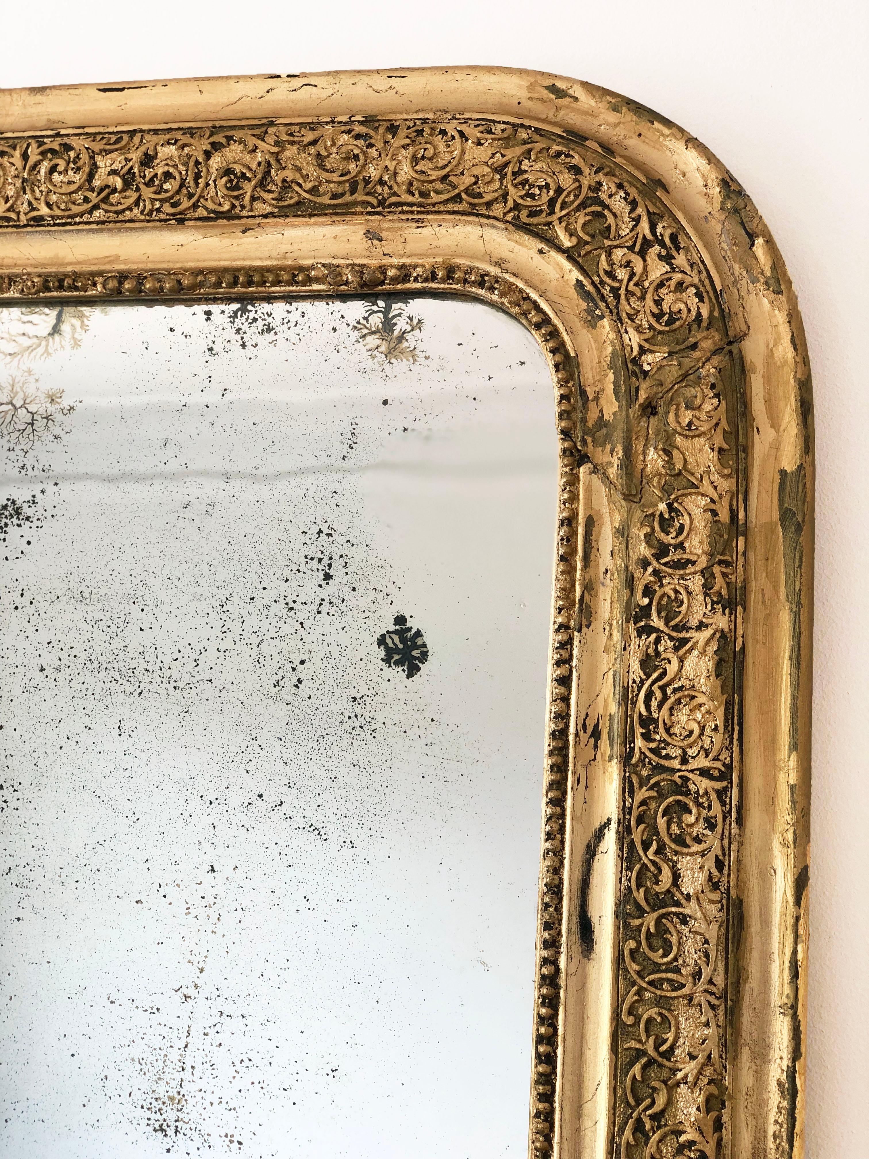 An antique Louis Philippe mirror from France, dating to the mid-19th century. The carved giltwood frame has an elegant, grand appearance with curved top corners, a beautifully worn gold leaf patina, and a delicate pearl rim. The original drawn glass