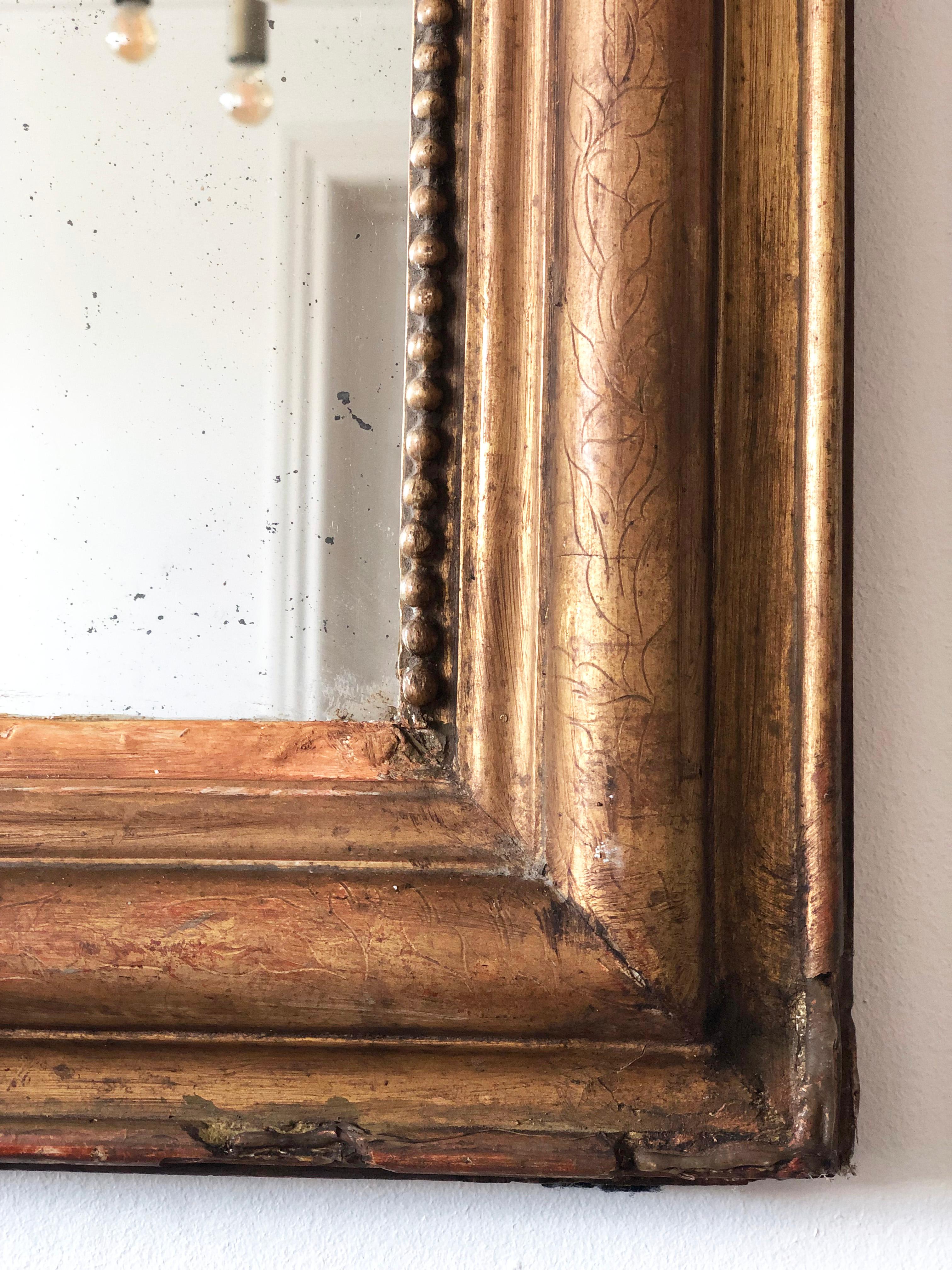 Miroir ancien Louis Philippe de France, datant de la fin du 19e siècle.
D'apparence grandiose, le cadre en bois doré sculpté présente des coins supérieurs gracieusement incurvés, une belle patine usée à la feuille d'or et un délicat rebord perlé. Le
