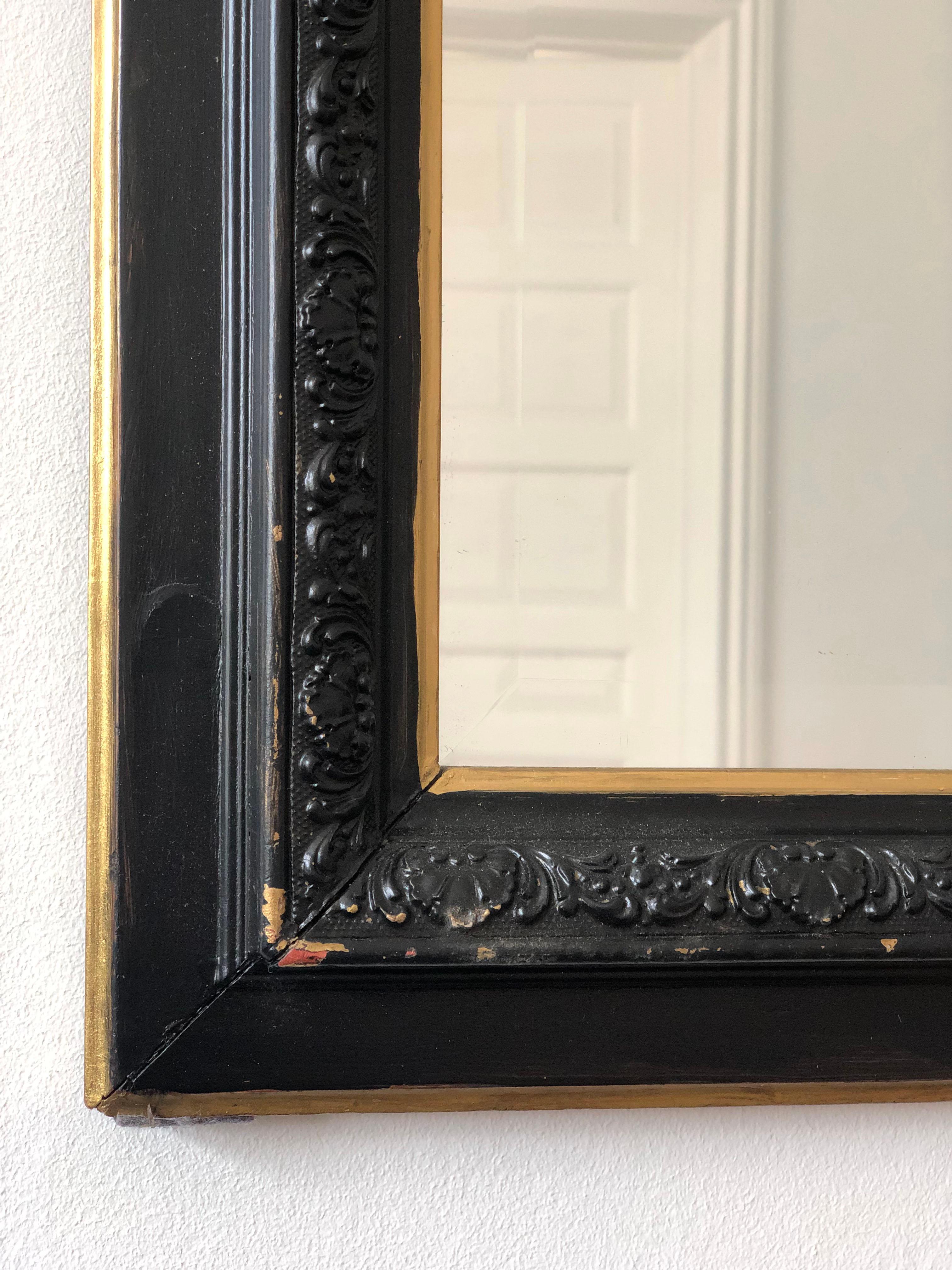 Antique French Louis Philippe mirror with beveled glass from the late 19th century. It has a black frame with soft gold trim and a curved top. The carved black edge gives the frame nice depth and detail. A timeless and elegant piece.

Object: