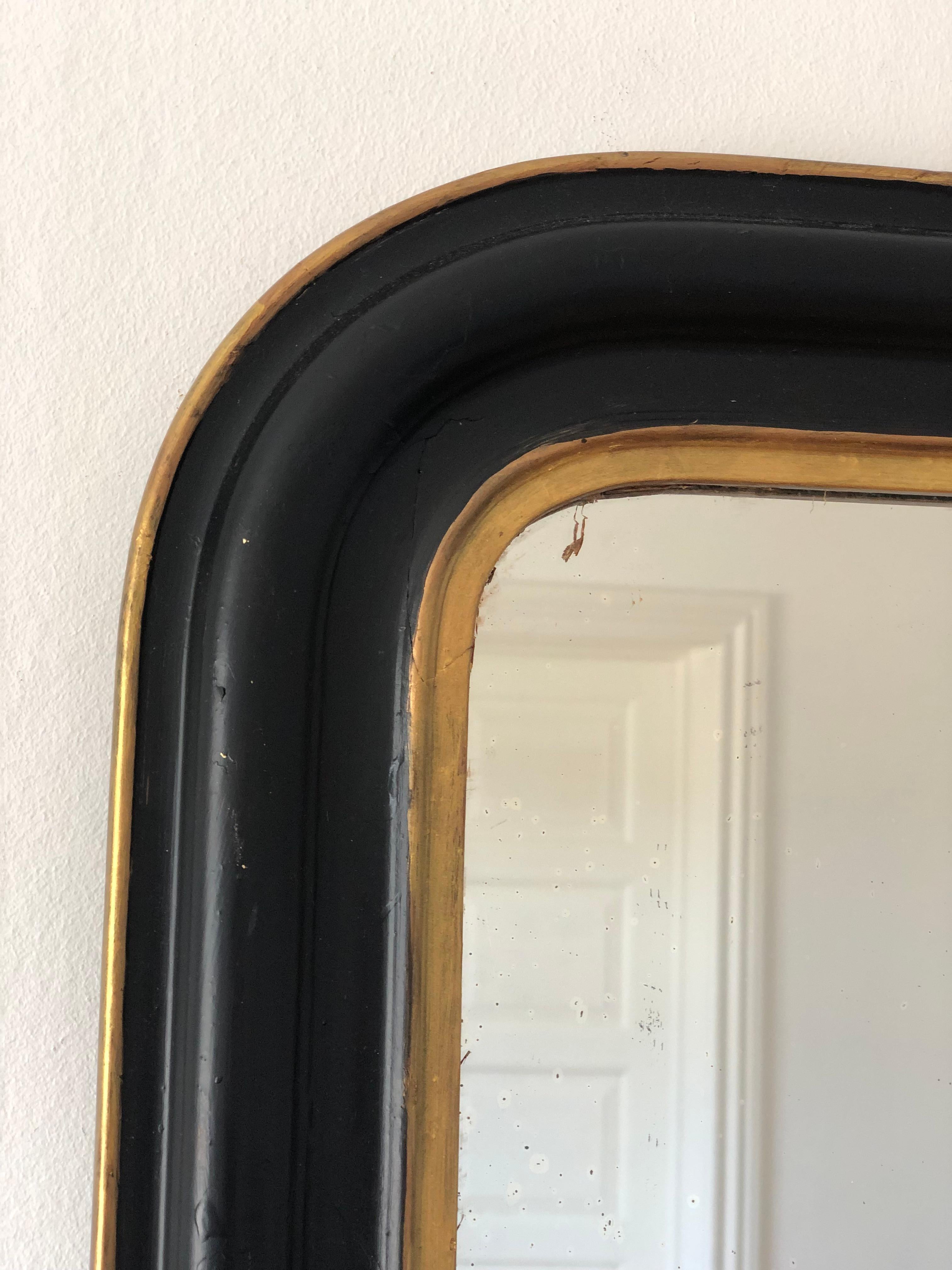 An enchanting antique Louis Philippe French mirror, dating to the late 19th century. The mirror features a refined black frame with a soft gold trim and a gracefully curved top, exuding timeless elegance and charm.

Object: mirror
Designer: a French
