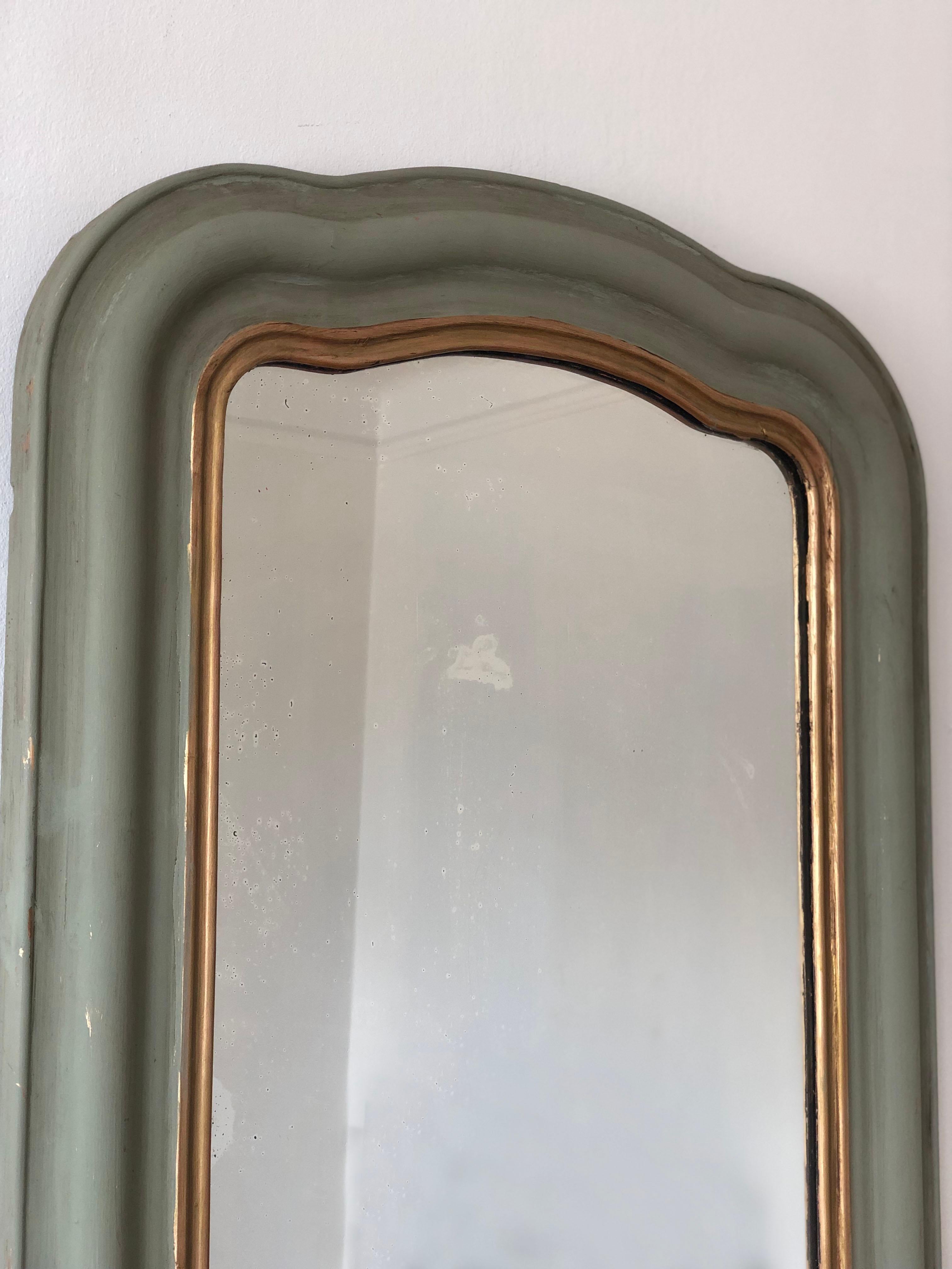 An enchanting antique Louis Philippe French mirror, dating to the late 19th century. The mirror features a refined green frame with a soft gold trim and a gracefully curved top, exuding timeless elegance and charm.

Object:  mirror
Designer: a