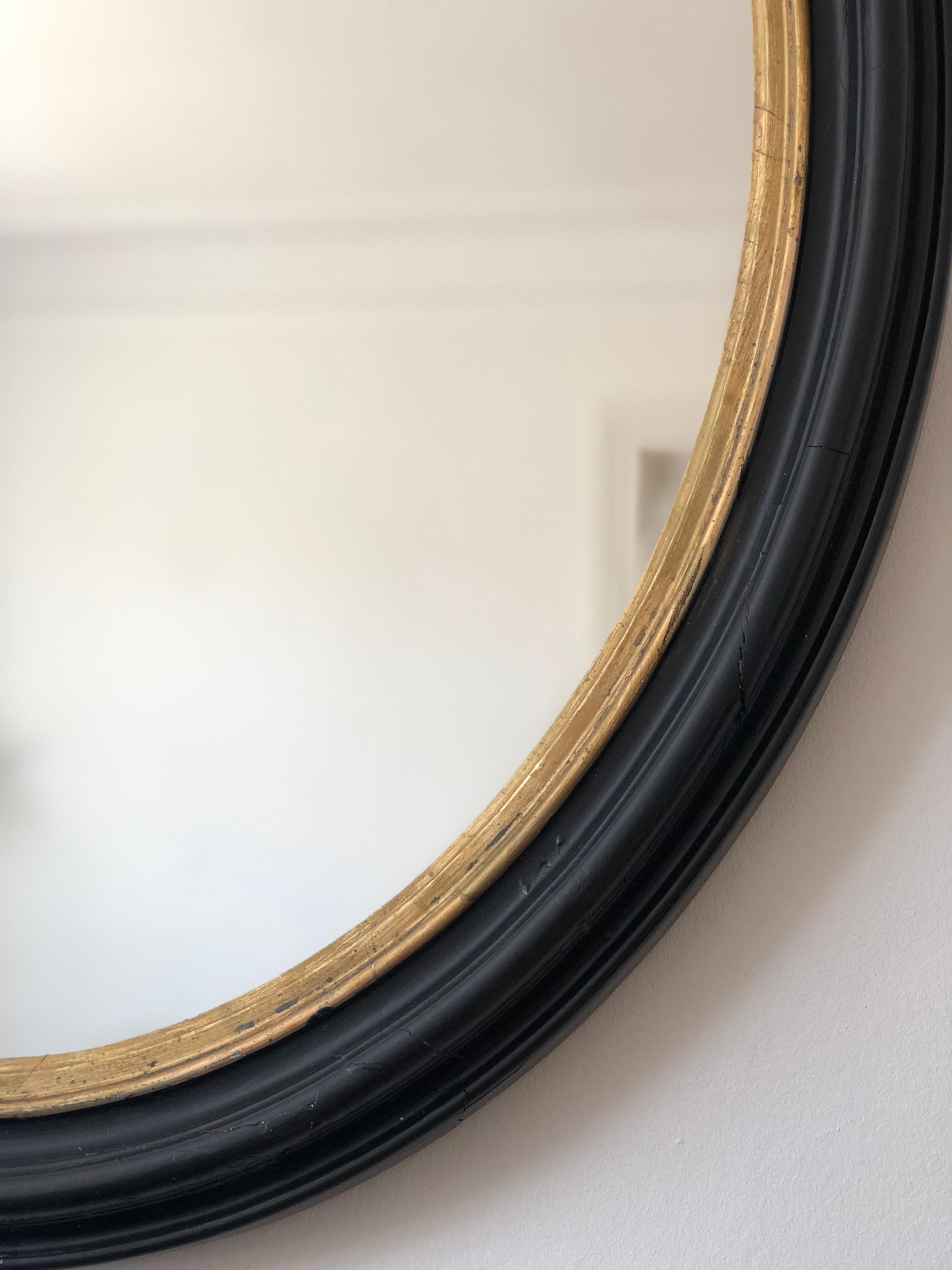 An enchanting antique Louis Philippe French mirror, dating to the late 19th century. The large oval mirror features a refined black frame with a soft gold trim, exuding timeless elegance and charm.

Object: mirror
Designer: a French artisan
Style: