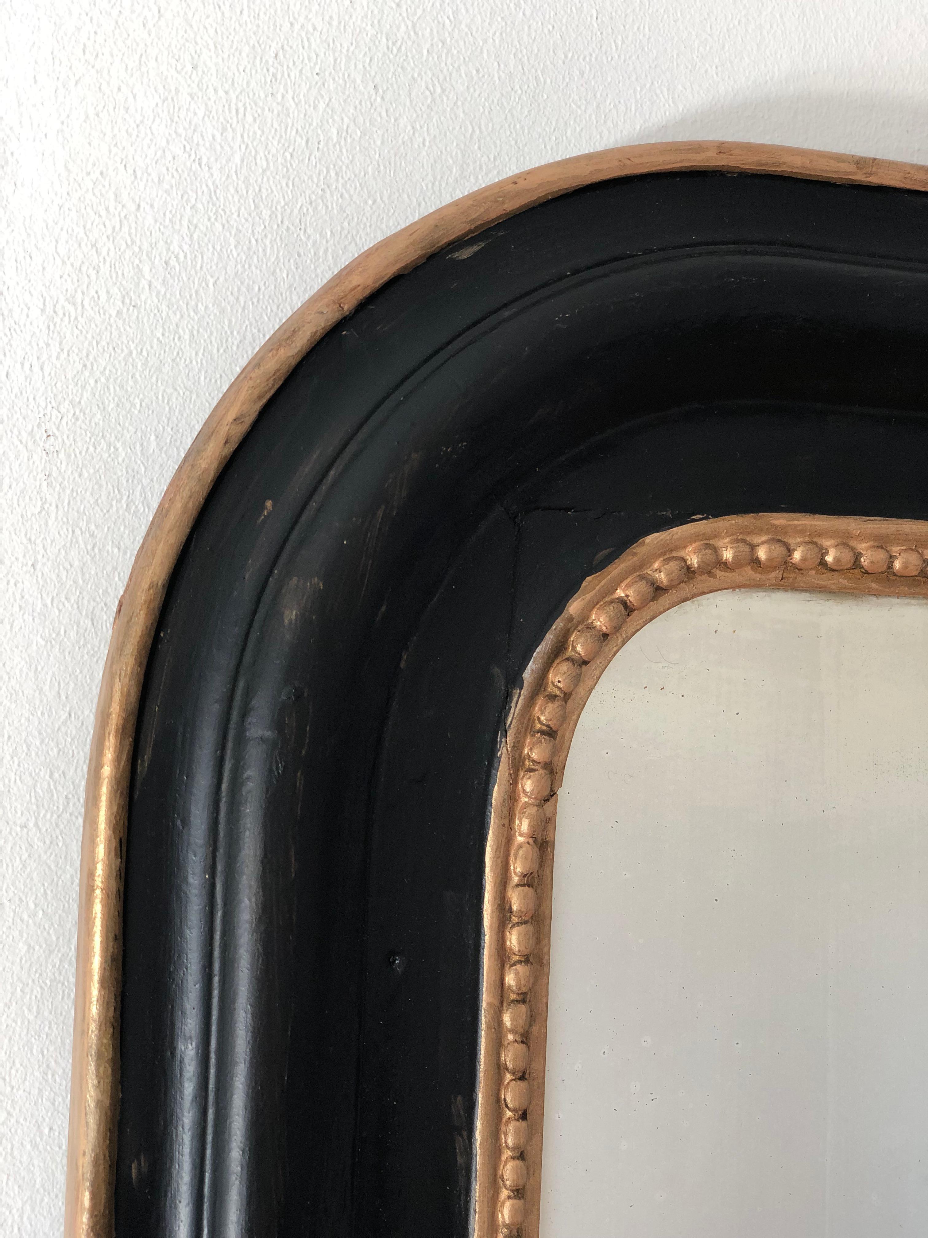 An enchanting original Louis Philippe mirror from France, dating to the late 19th century. The mirror features a refined black frame with a gold pearl rim, mercury glass, and a gracefully curved top, exuding timeless elegance and charm.

Object: