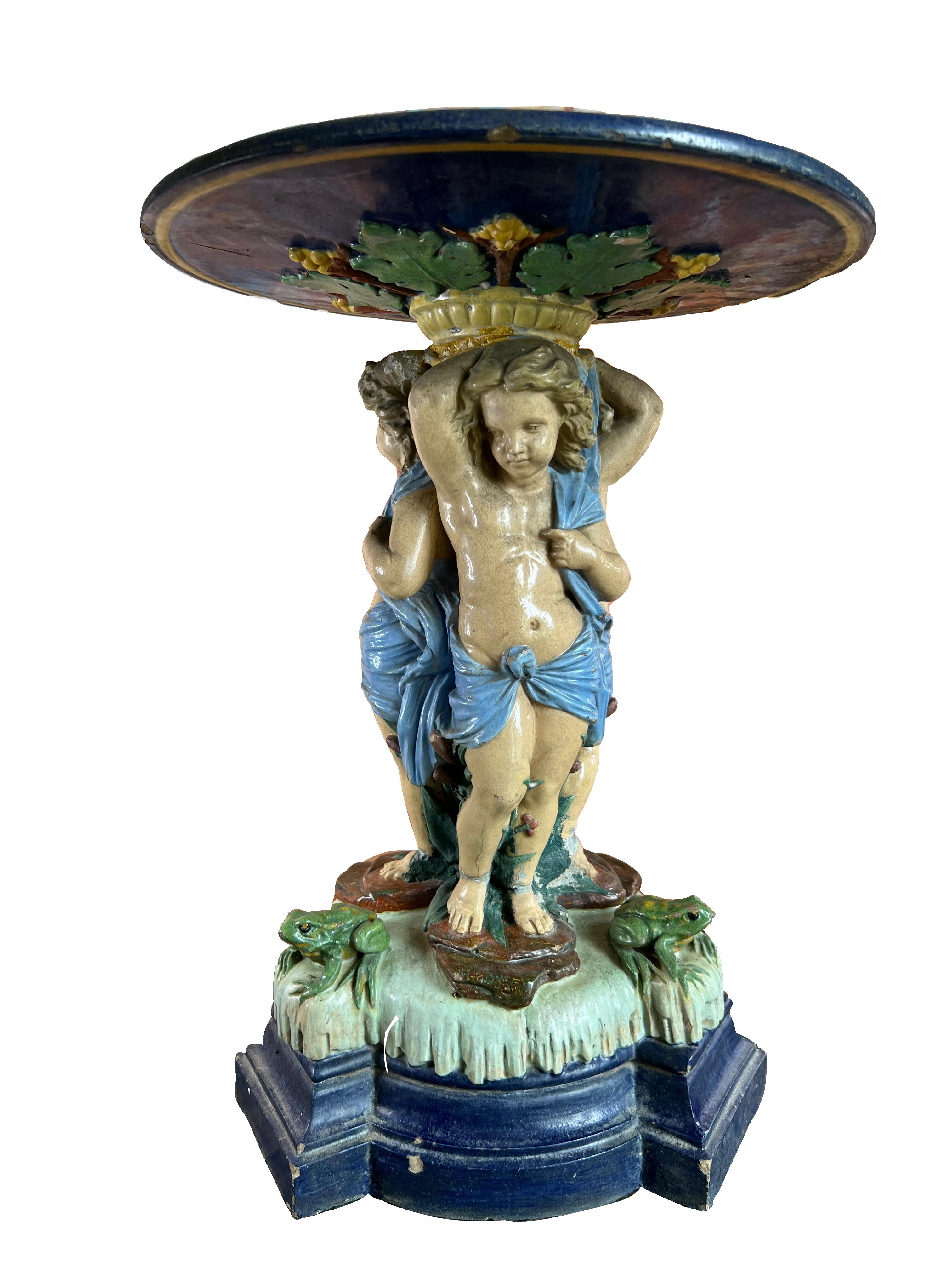 This large French majolica centerpiece, hand-painted and featuring three putti carrying a platter, is an exceptional piece from the 19th century, in the style of Palissy, Minton, and Royal Dux. Likely originating from France or Italy, this