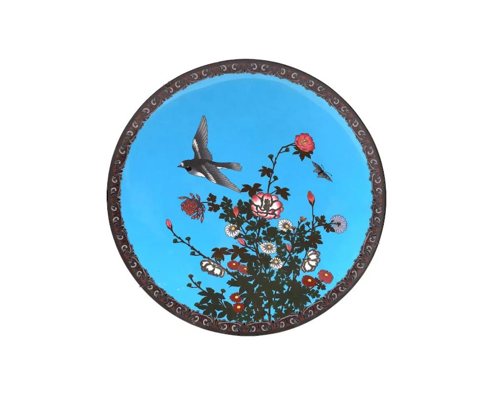 A large antique Japanese, late Meiji era, enamel over copper charger plate. The plate is adorned with a polychrome enamel image of a bird flying over blossoming flowers on the turquoise ground made in the Cloisonne technique. The backside is