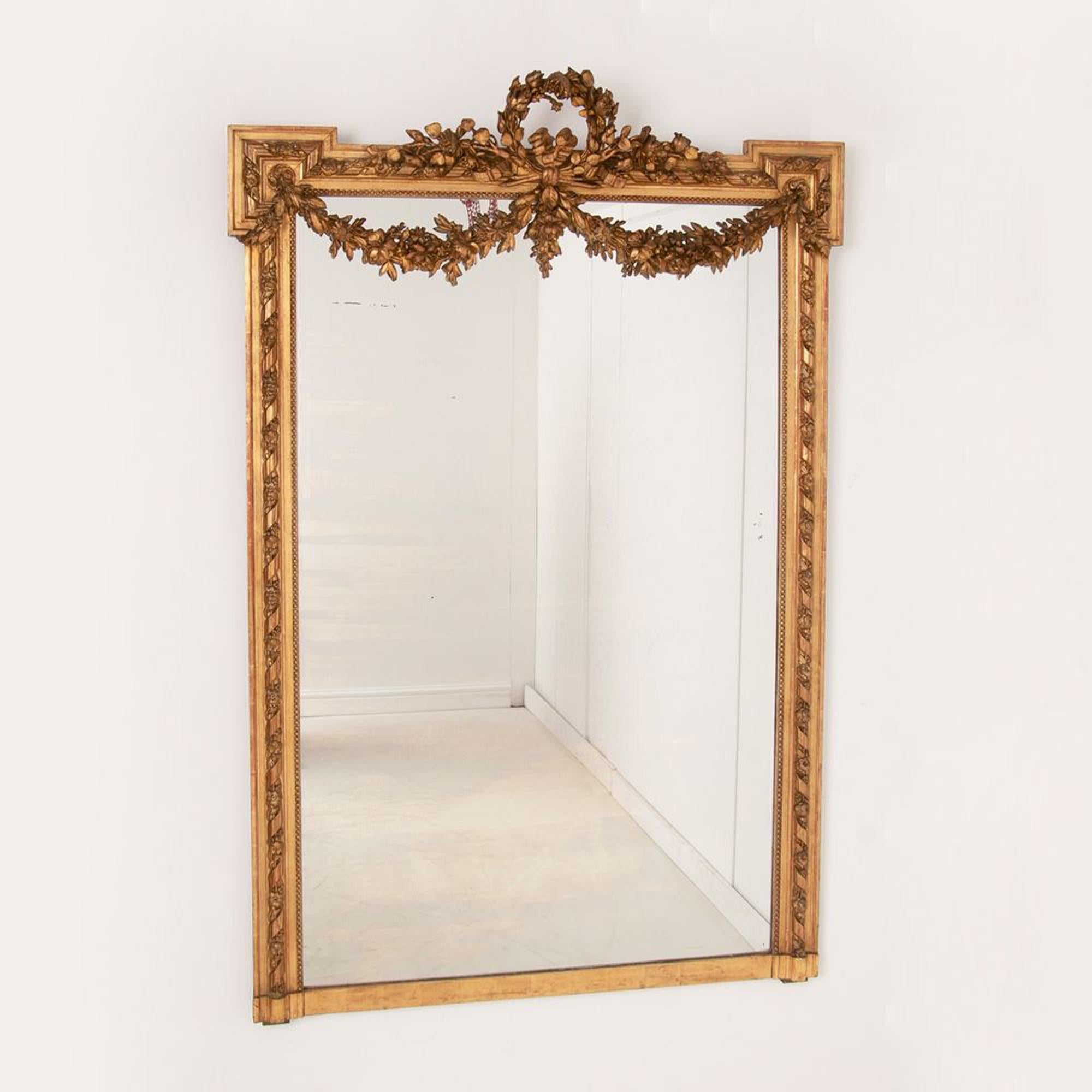 Großer vergoldeter auf rotem Louis XVI-Stil antiker Spiegel mit Gesso-Wappen, Schwänzen und Band mit Blumendekoration am Rahmen. In der originalen zweifarbigen Vergoldung, die stellenweise auf Rot abgenutzt ist. Originales, leicht patiniertes Glas.
