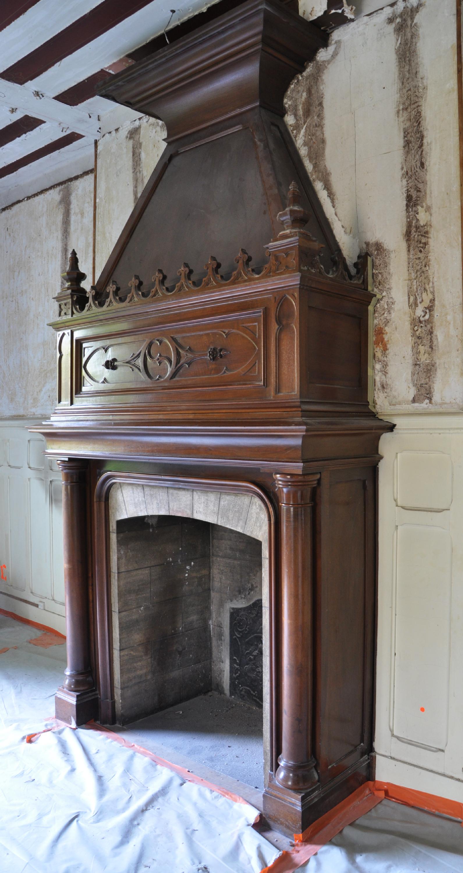 This large Neo-Gothic style fireplace with hood was made at the end of the 19th century out of beautiful walnut wood. The jambs with semi-detached columns support a wide entablature. The carved decoration of the entablature is typical of the