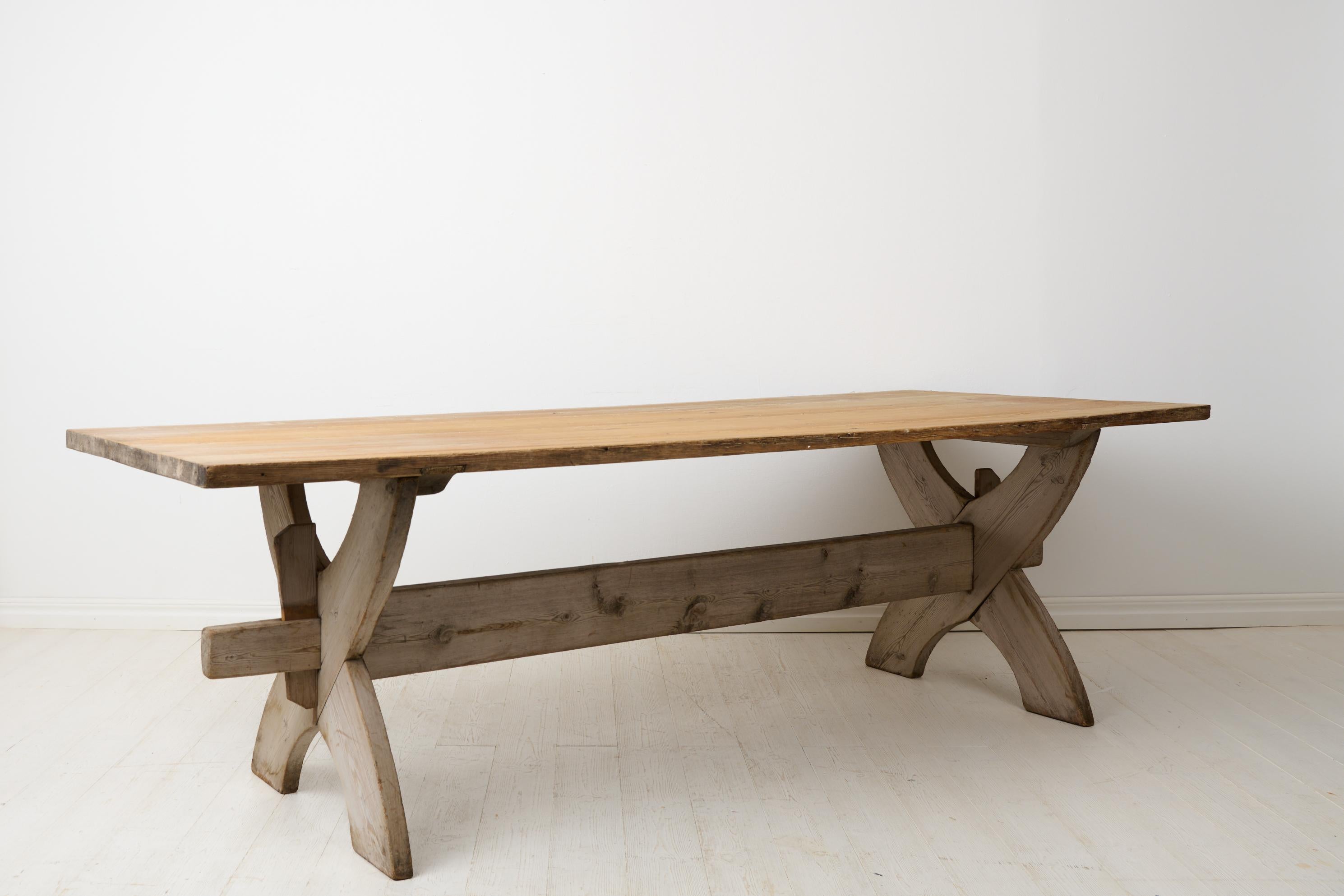 Large antique dining table or trestle table from northern Sweden made during the early 1800s. The table has a thick, solid table top made with just three boards. The leg-frame has slightly s-shaped trestles and the two – table top and leg-frame –