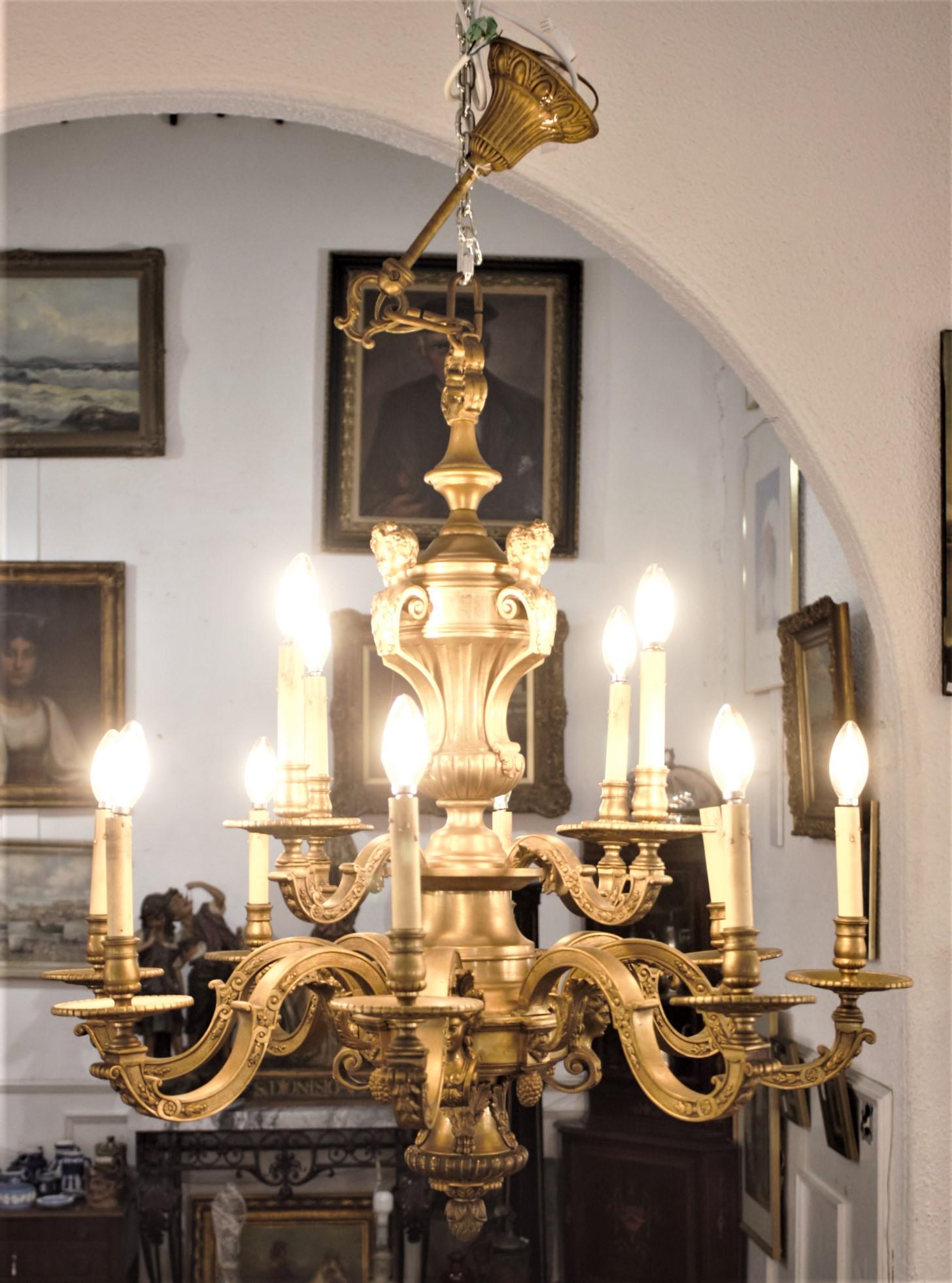 Dieser sehr große und massive zwölfarmige Kronleuchter aus gegossener und vergoldeter Bronze wurde um 1900 in Frankreich im Louis-XIV-Stil hergestellt. Der Kronleuchter ist kunstvoll mit einer Reihe von figuralen Köpfen auf der Spitze gegossen, die