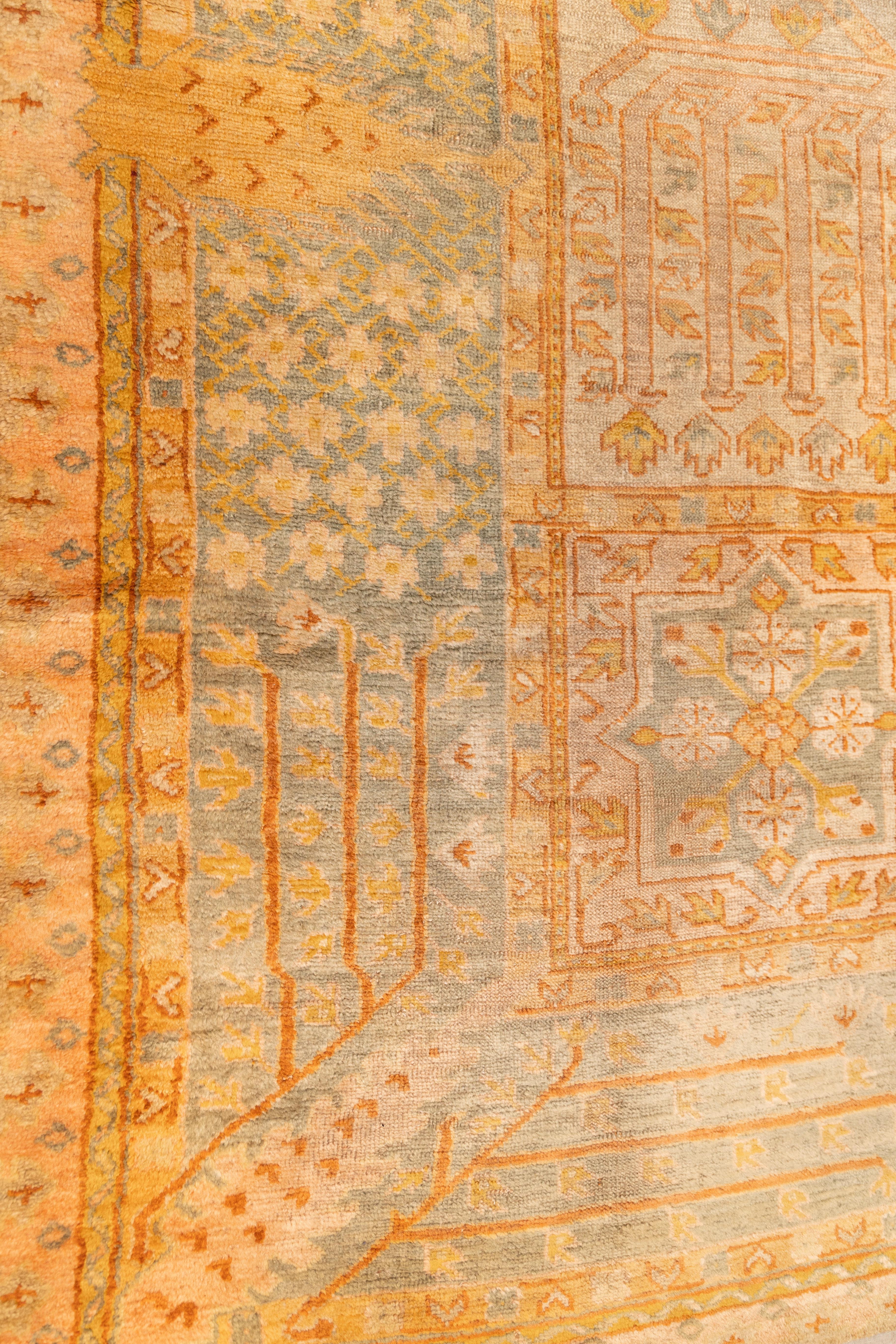 early 20th-century Oushak carpet inspired by persian garden designs featuring a structured layout of large rectangular compartments arranged symmetrically across the field. Each compartment contains variations of stylized floral, geometric, and