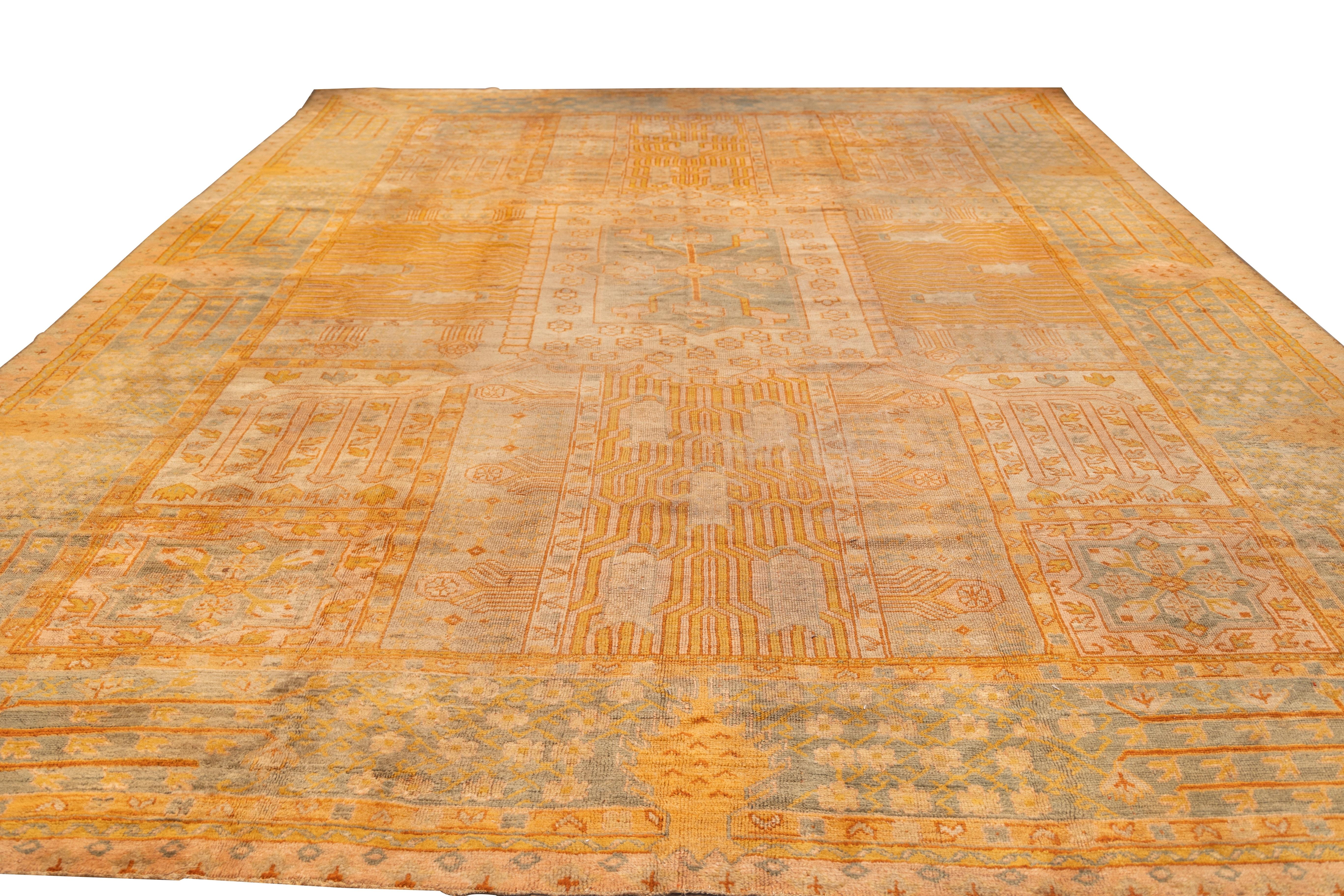 early 20th-century Oushak carpet inspired by persian garden designs featuring a structured layout of large rectangular compartments arranged symmetrically across the field. Each compartment contains variations of stylized floral, geometric, and