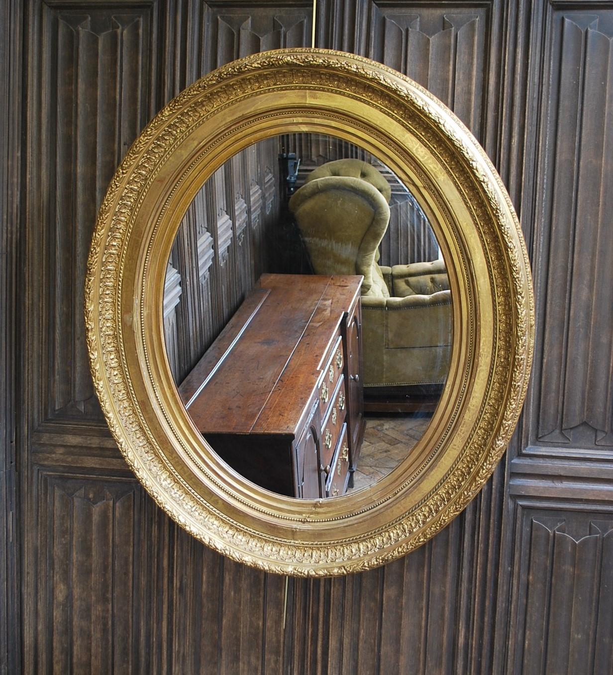 Hutton-Clarke Antiques is delighted to present a magnificent Large Antique Oval Gilded Mirror. This exquisite mirror boasts a deep concave molded frame adorned with a wreath motif along its exterior edge, while traditional moldings grace its