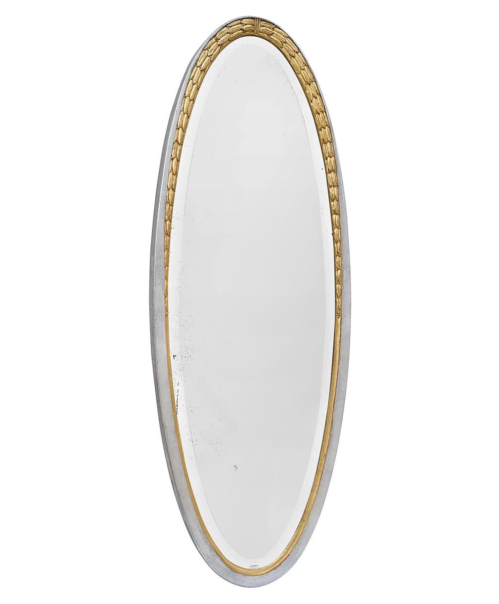 Très grand miroir ovale Art Déco français à décor de feuilles de laurier, datant de 1928. Magnifique cadre ovale ancien en bois sculpté doré et argenté (Redorure à la feuille par l'ATELIER RTCD Paris). Largeur du cadre antique :  5,5 cm / 2,16 in.