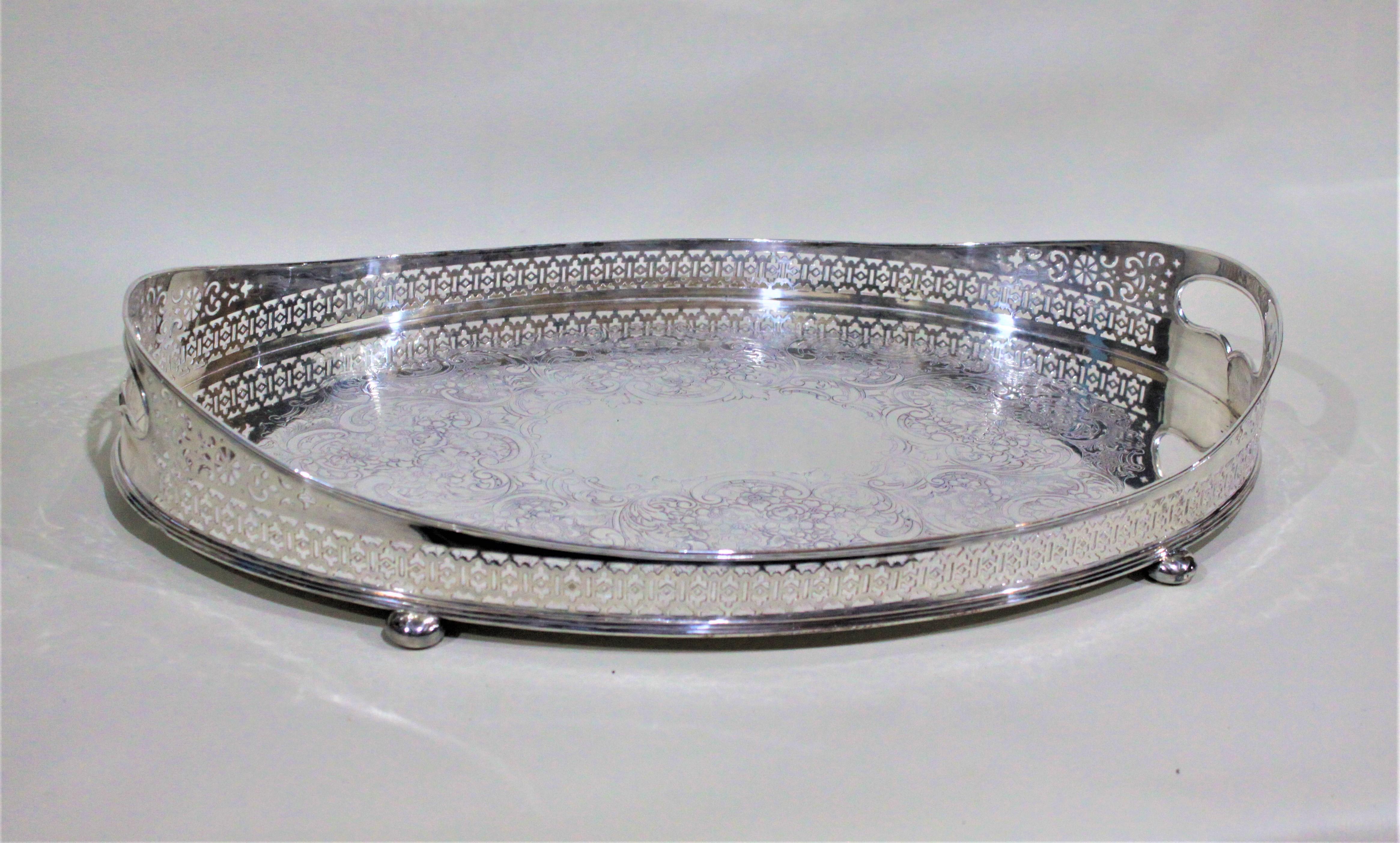 This large oval silver plated gallery serving tray is unmarked, but presumed to be made in England during the 1920s in the style of the Victorian Period. The tray has an ornately pierced gallery surround with handles fashioned into either end. The