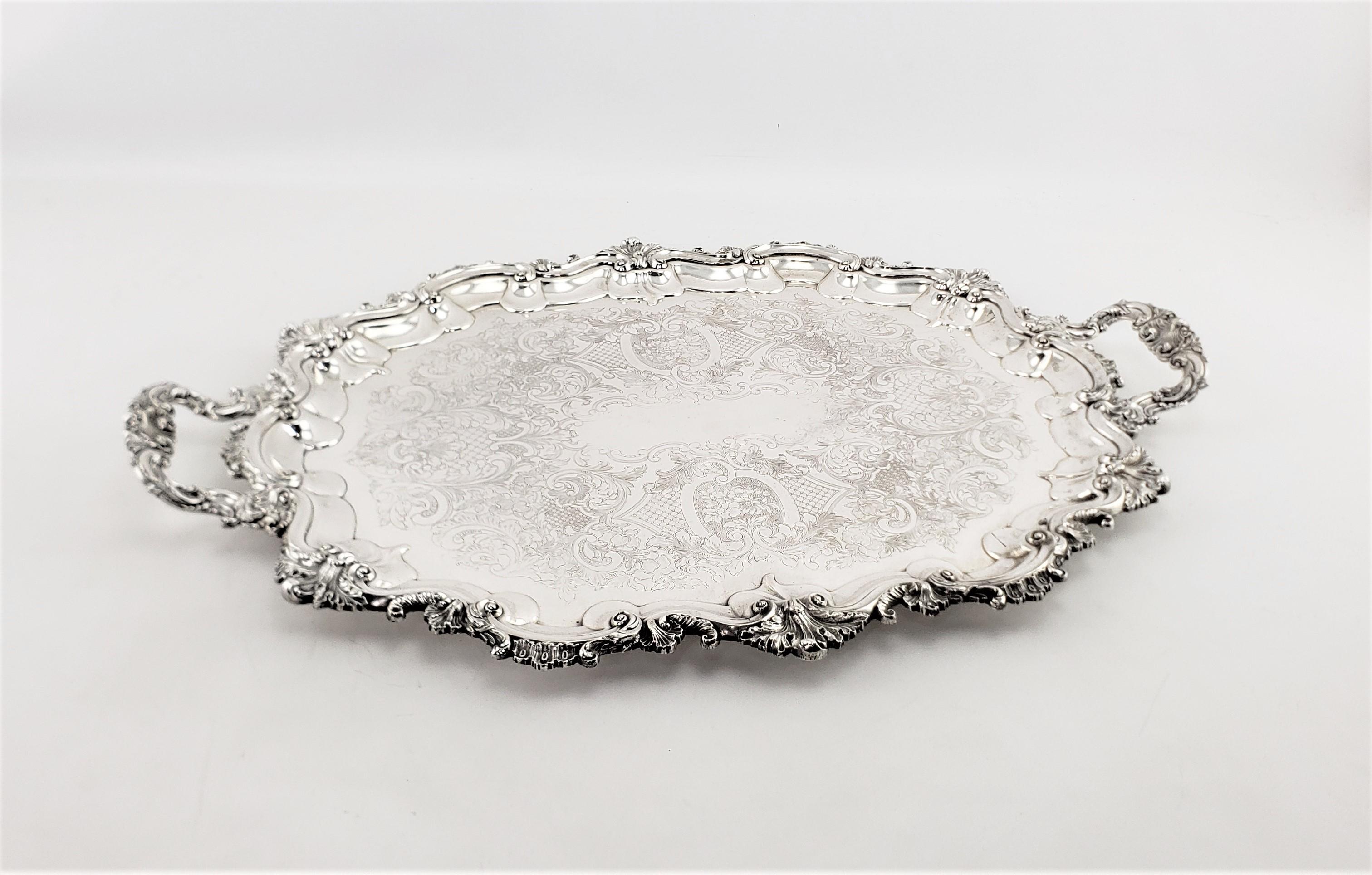 This large antique silver plated oval serving tray originates from England and made in approximately 1920 in a Victorian style. The tray has very ornate stylized floral decoration on the entire surround which is accented on the handles. The surface