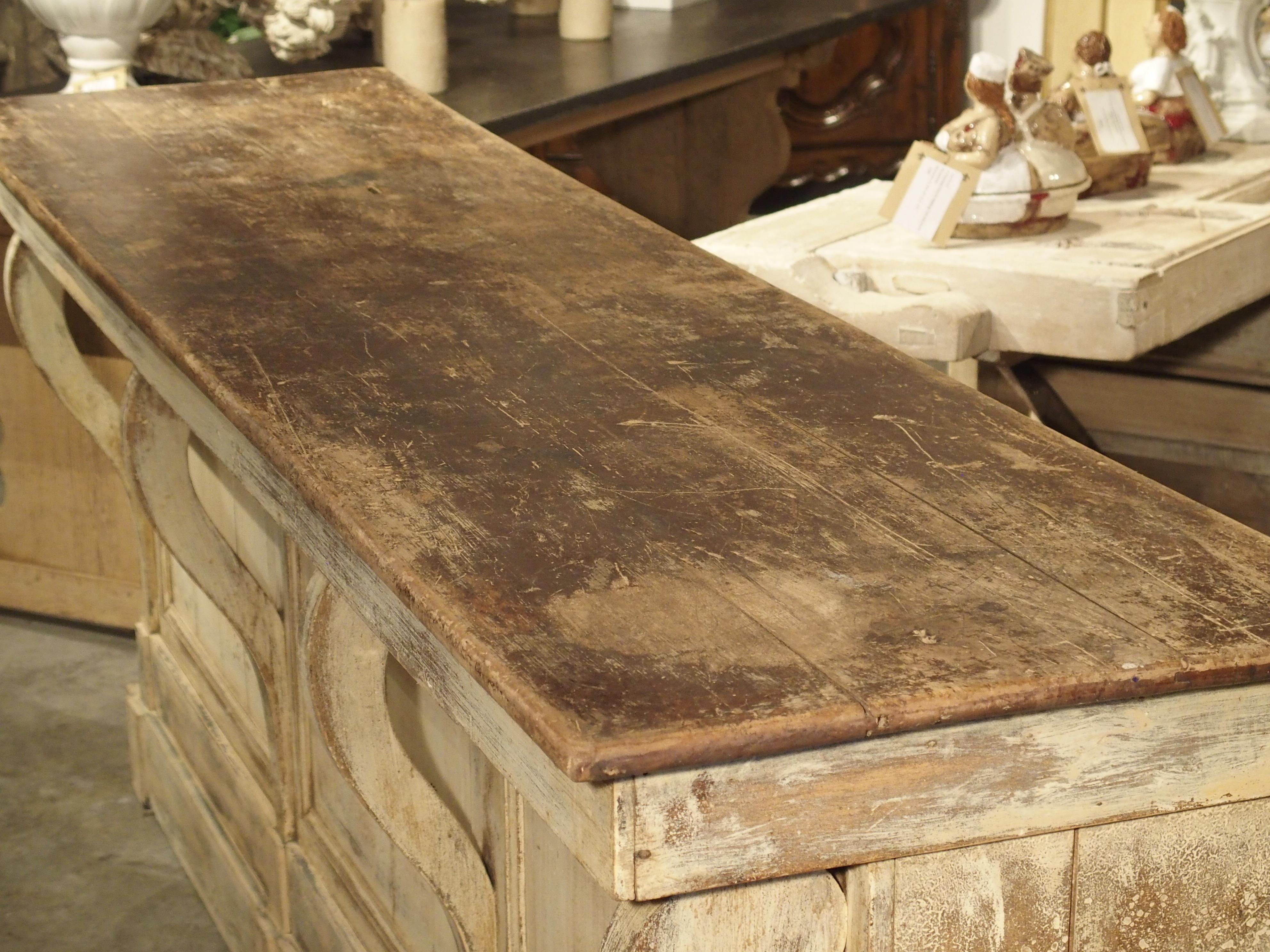 This is an impressive and large shop counter from France, dating to the second half of the 1800s. The original, distressed cream paint is nicely contrasted by the brown stained top, while the 4 gracefully scrolling pilasters are elevated by a double