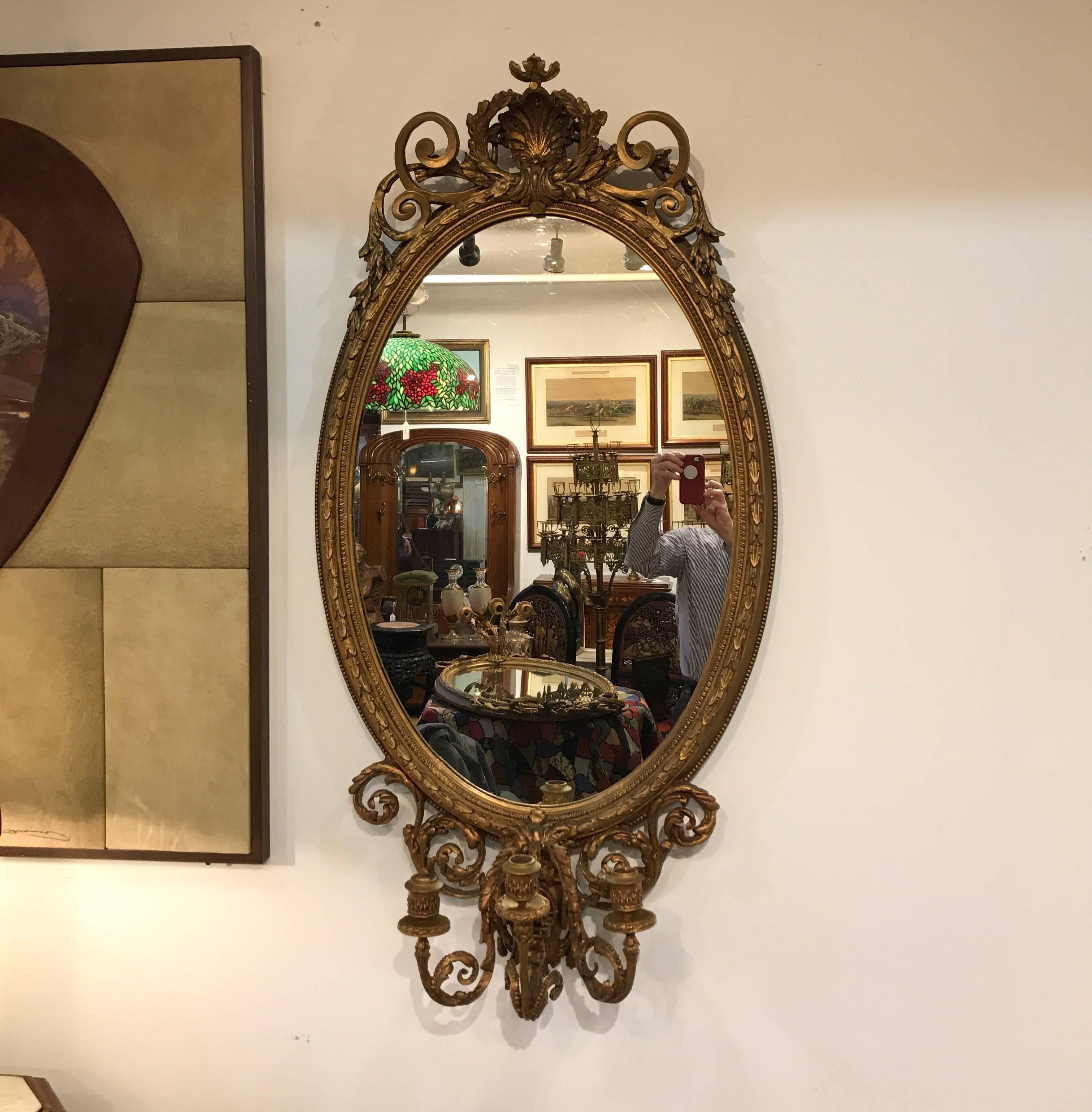 Large pair of oval mirrors with candelabra fronts. The pair with detailed tops and bottoms with beaded detail along the sides. The bottoms with three arms for candles. A rare 19th century pair. Some fade to silvering on one mirror.