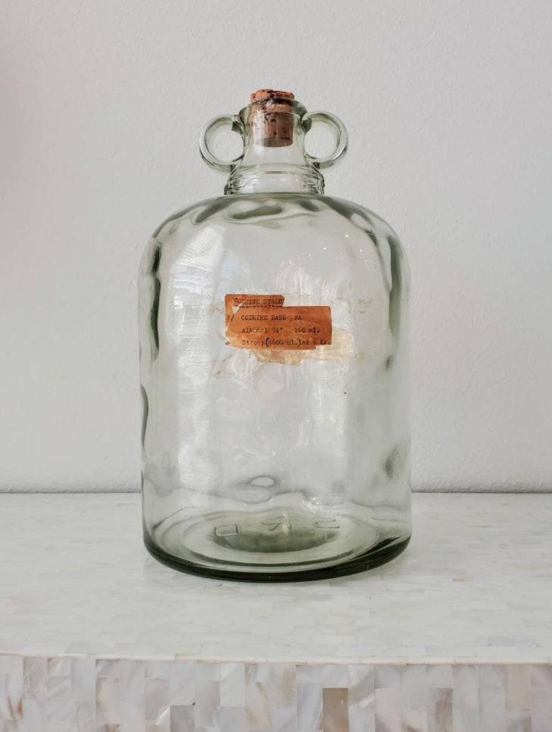 A highly collectible and decorative, unusually large, heavy-duty antique English clear glass pharmaceutical medication bottle from the early 20th century. 

Used by chemists, pharmacists and medical doctors, the industrial quality and quantity