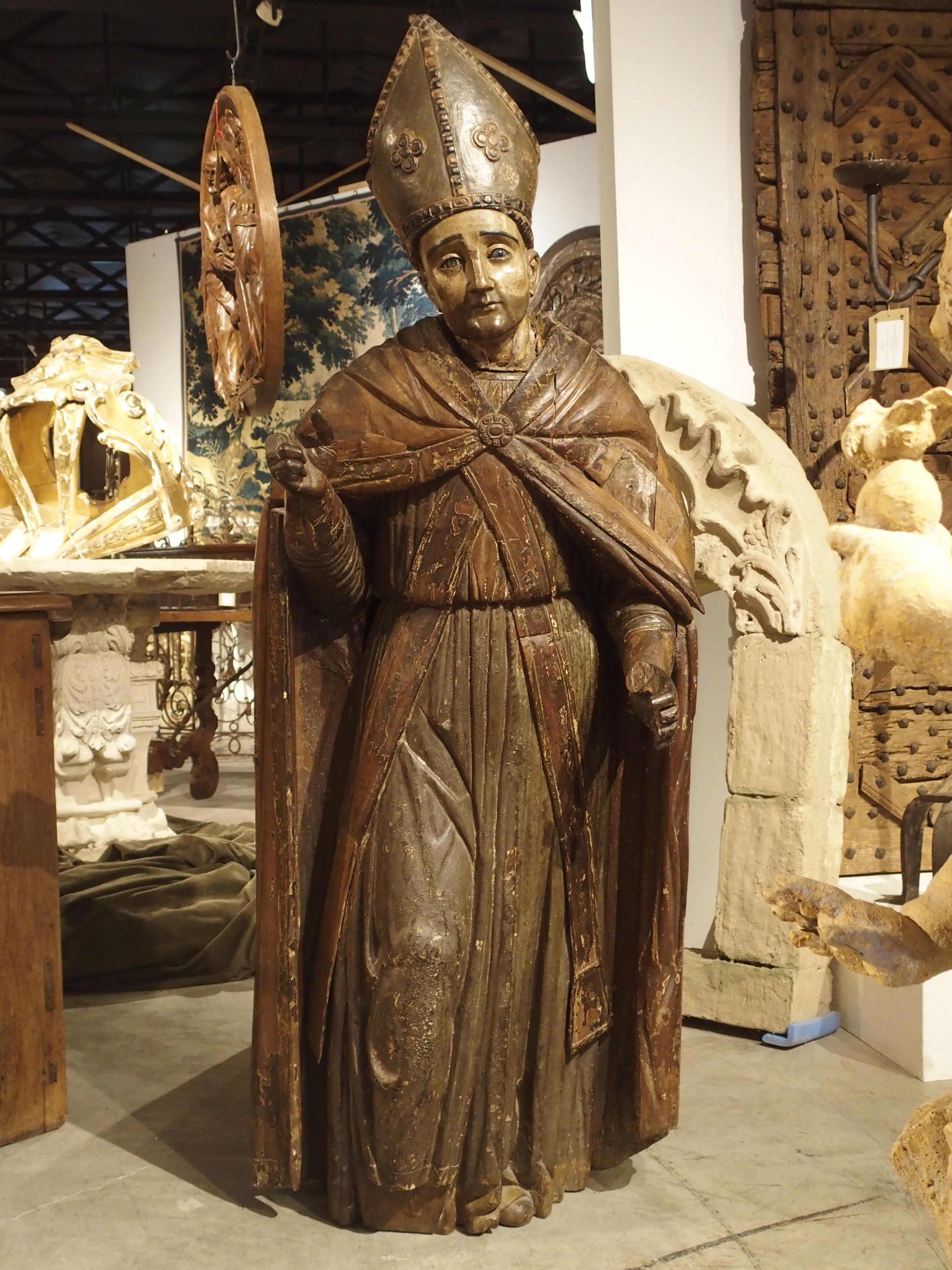 This 64 inch high antique statue of a Bishop dates to circa 1650 and is German in origin. Starting in the 15th and 16th centuries, there was a large demand for ecclesiastical carvings throughout central and western Europe. Large statues were