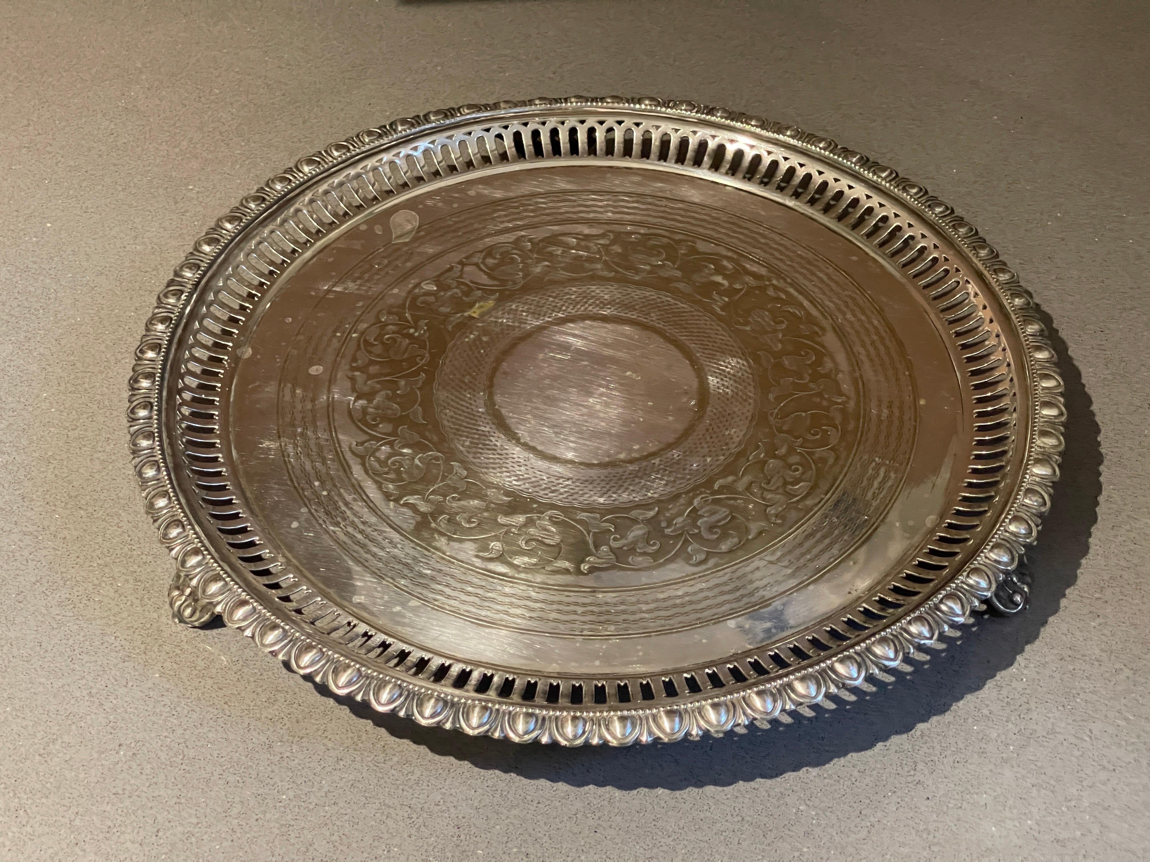 This large antique silver plated serving tray was made by a well-known company in England and dates to approximately 1920 and was done in a Victorian style. The tray is ornately decorated along the sides with stylized shells and leaves which are