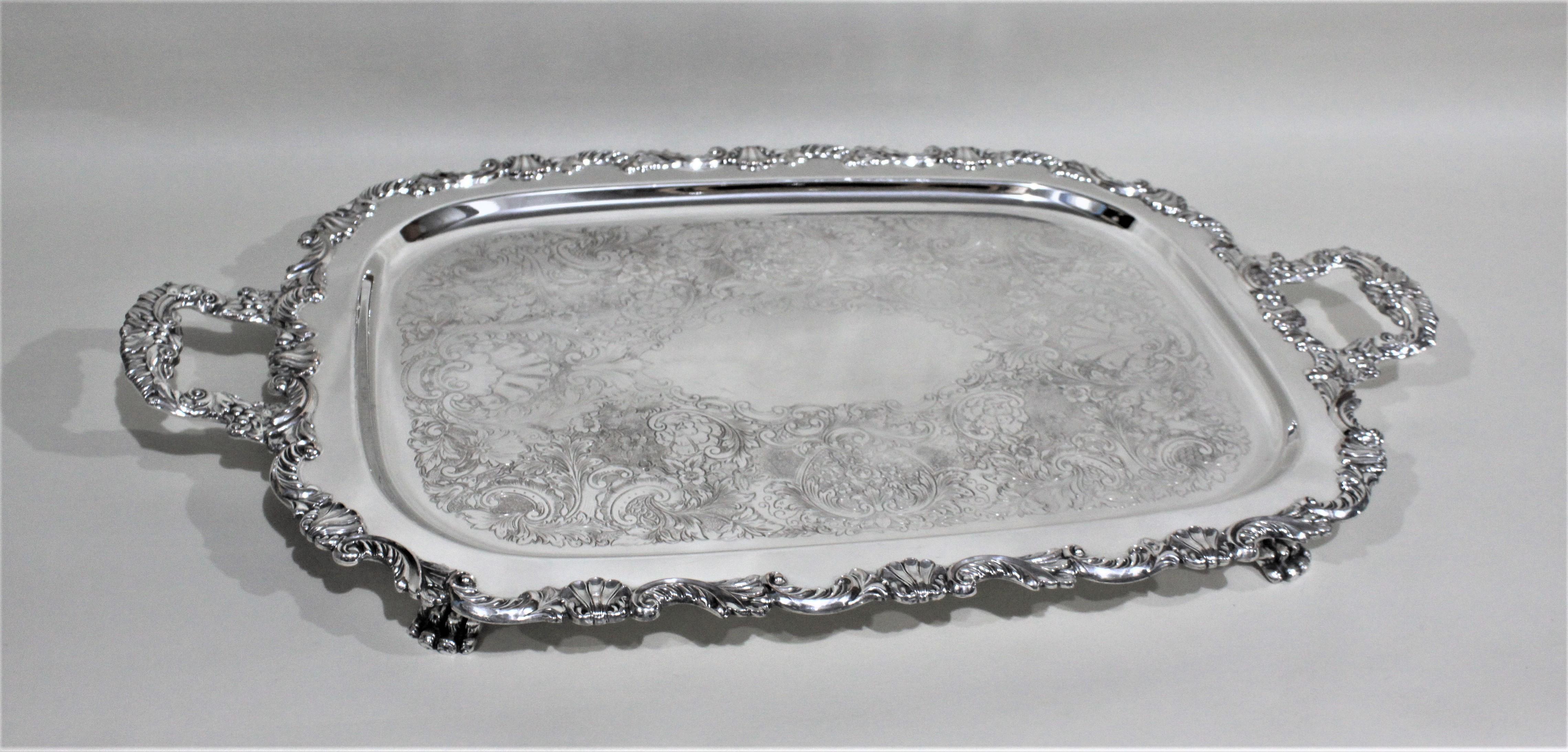 This large and rectangular shaped silver plated serving tray is presumed to have been made in England between 1900 and the 1920 time and has been done in the Victorian style. The tray has very ornate handles and surround and is intricately engraved