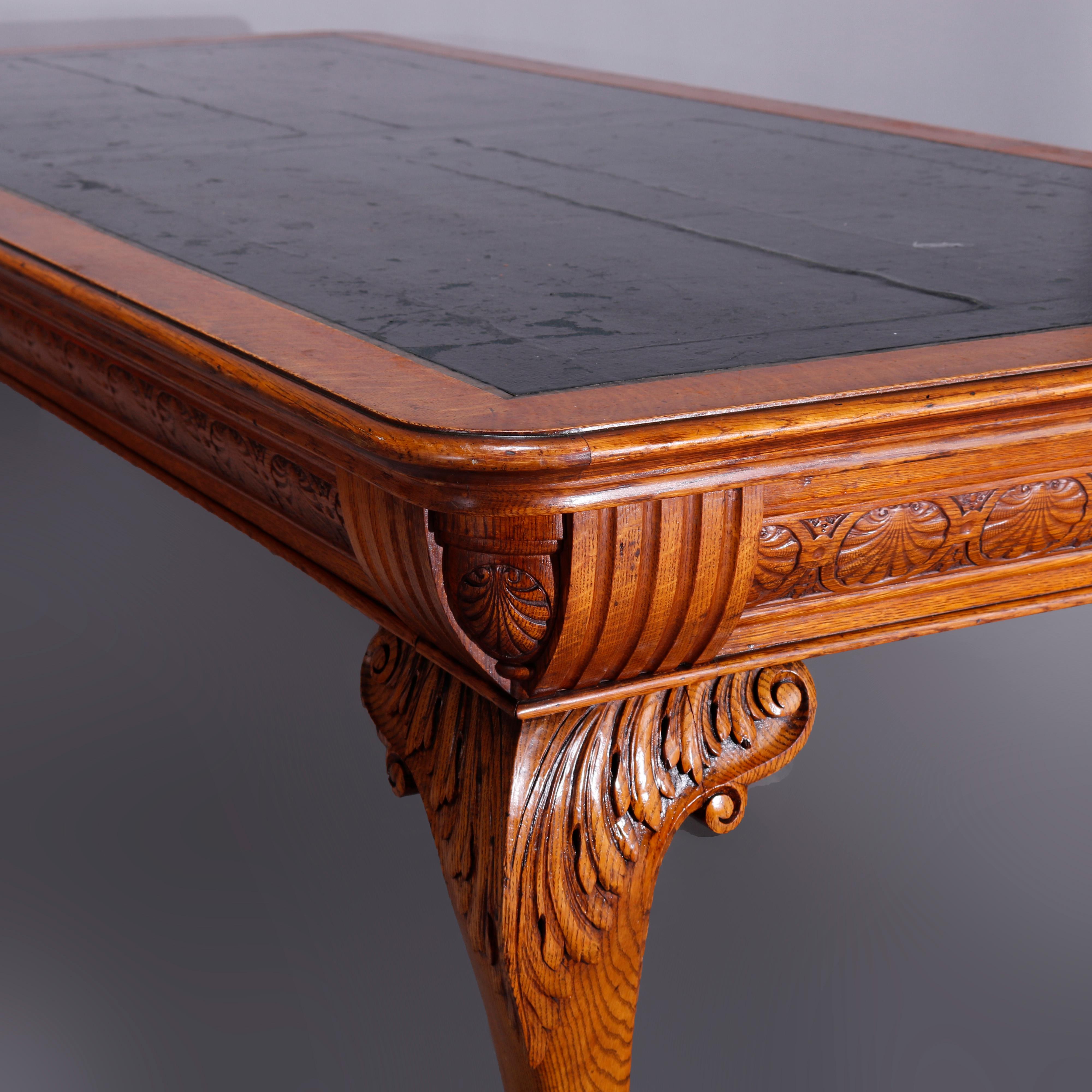 An antique conference table in the manner of RJ Horner School offers oak construction with top having leather inset and deep skirt with repeating carved foliate and palmette elements, raised on cabriole legs with carved acanthus knees and scroll