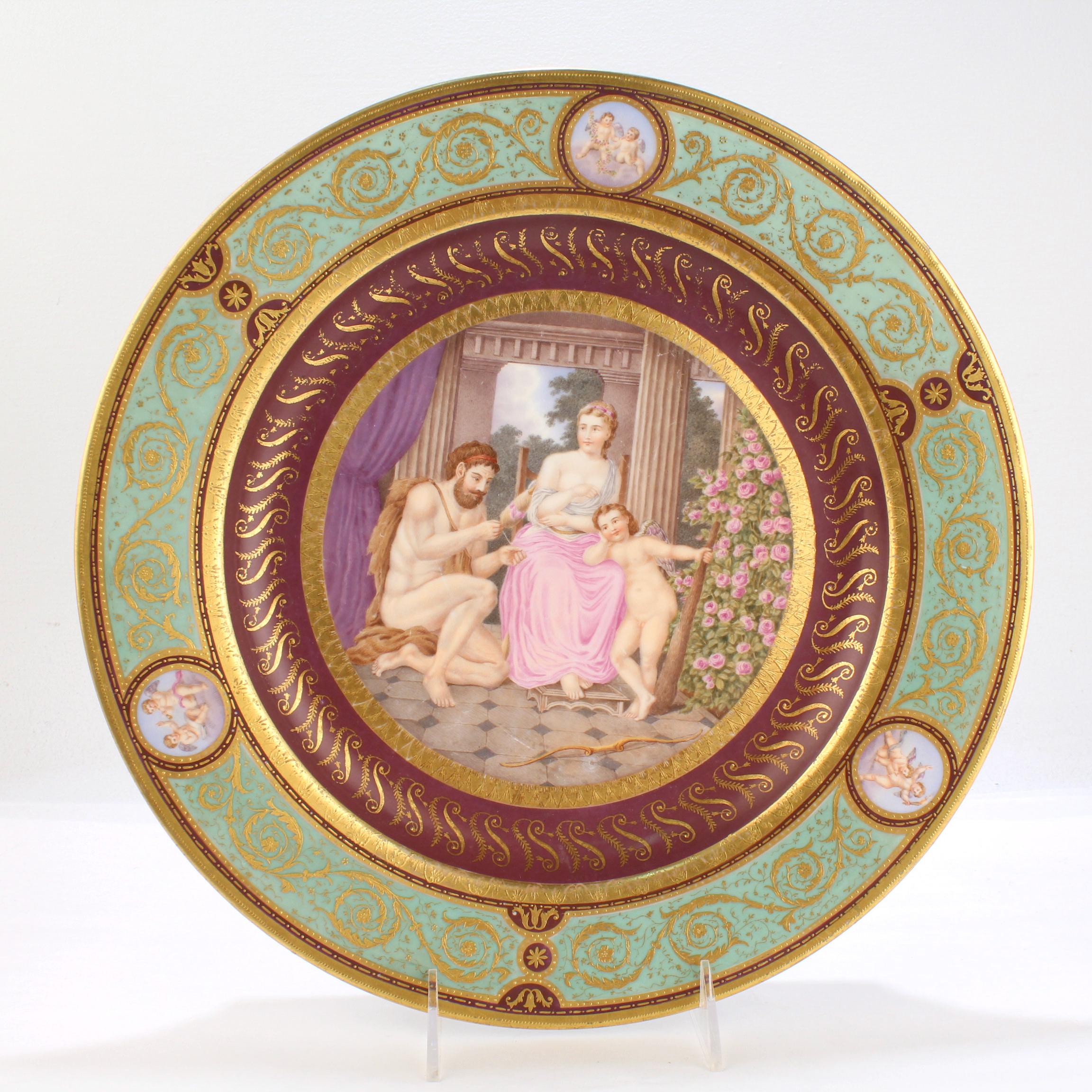 A fine antique Royal Vienna porcelain charger.

Hand painted with a mythological scene including a spinner or weaver, a man with a bear skin cloak, and Cupid. We're not sure of the allegory (but clearly this relates to ancient
