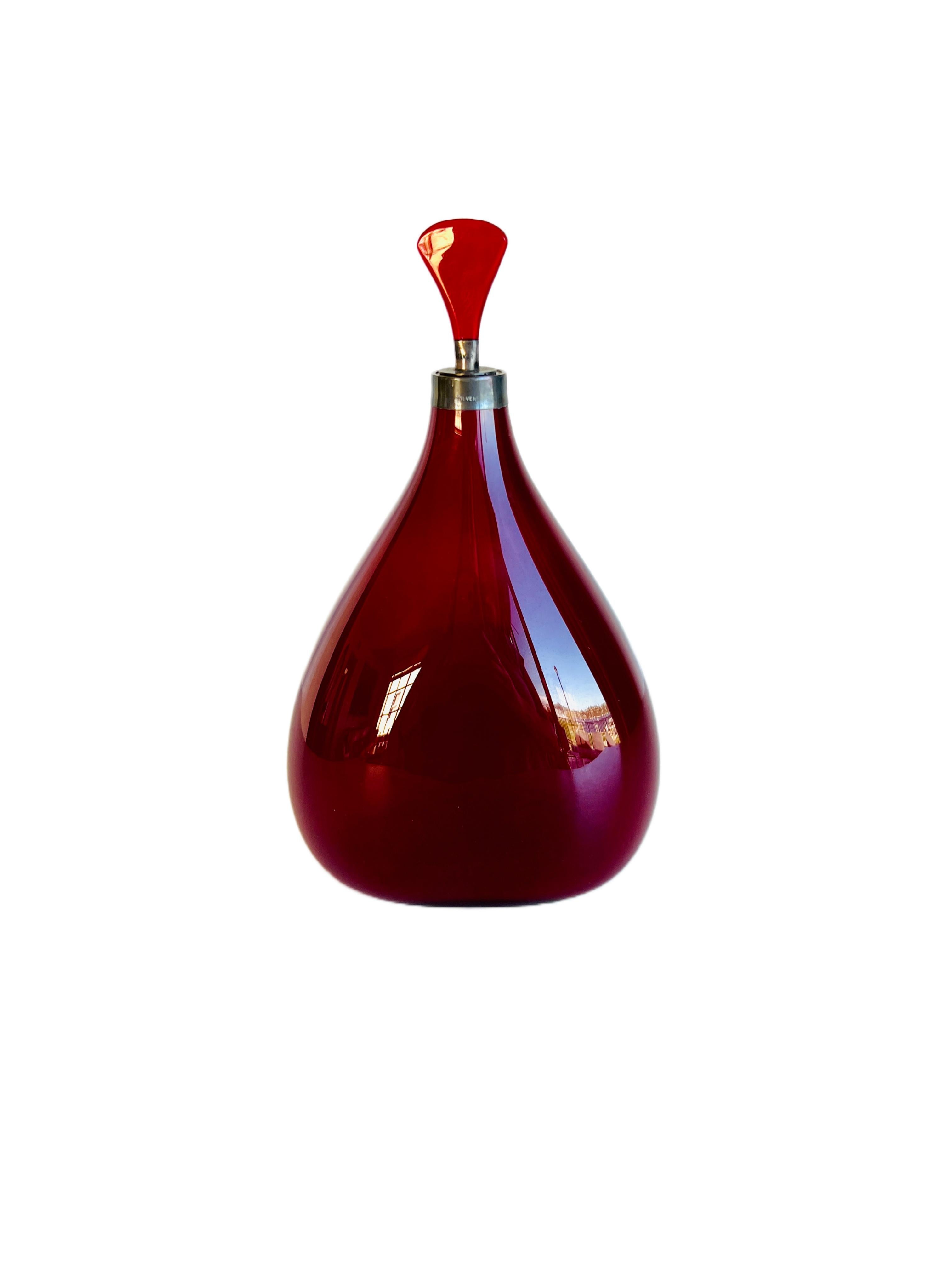 Cette charmante bouteille est assez grande, puisqu'elle mesure 7 pouces de haut. Il est d'une belle couleur rouge rubis presque opaque. Il n'y a pas de coutures dans la bouteille. Il n'y a qu'une couture dans la bouche d'argent. Le bouchon est en