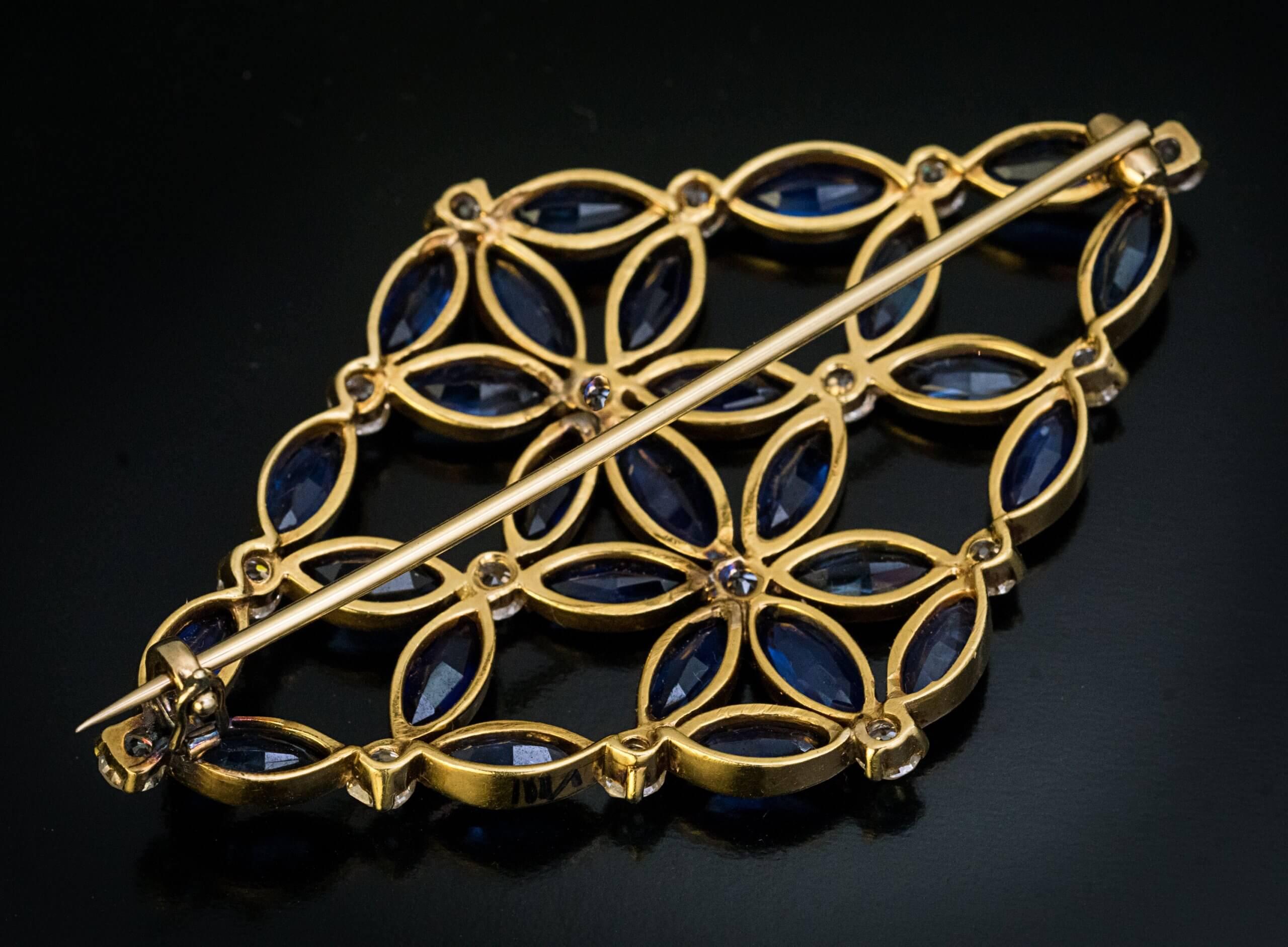 Circa 1910s  This one of a kind floral motif late Art Nouveau / early Art Deco era brooch is superbly modeled and finely crafted in 18K yellow gold. The brooch is set with twenty seven marquise cut blue sapphires and sixteen old brilliant cut