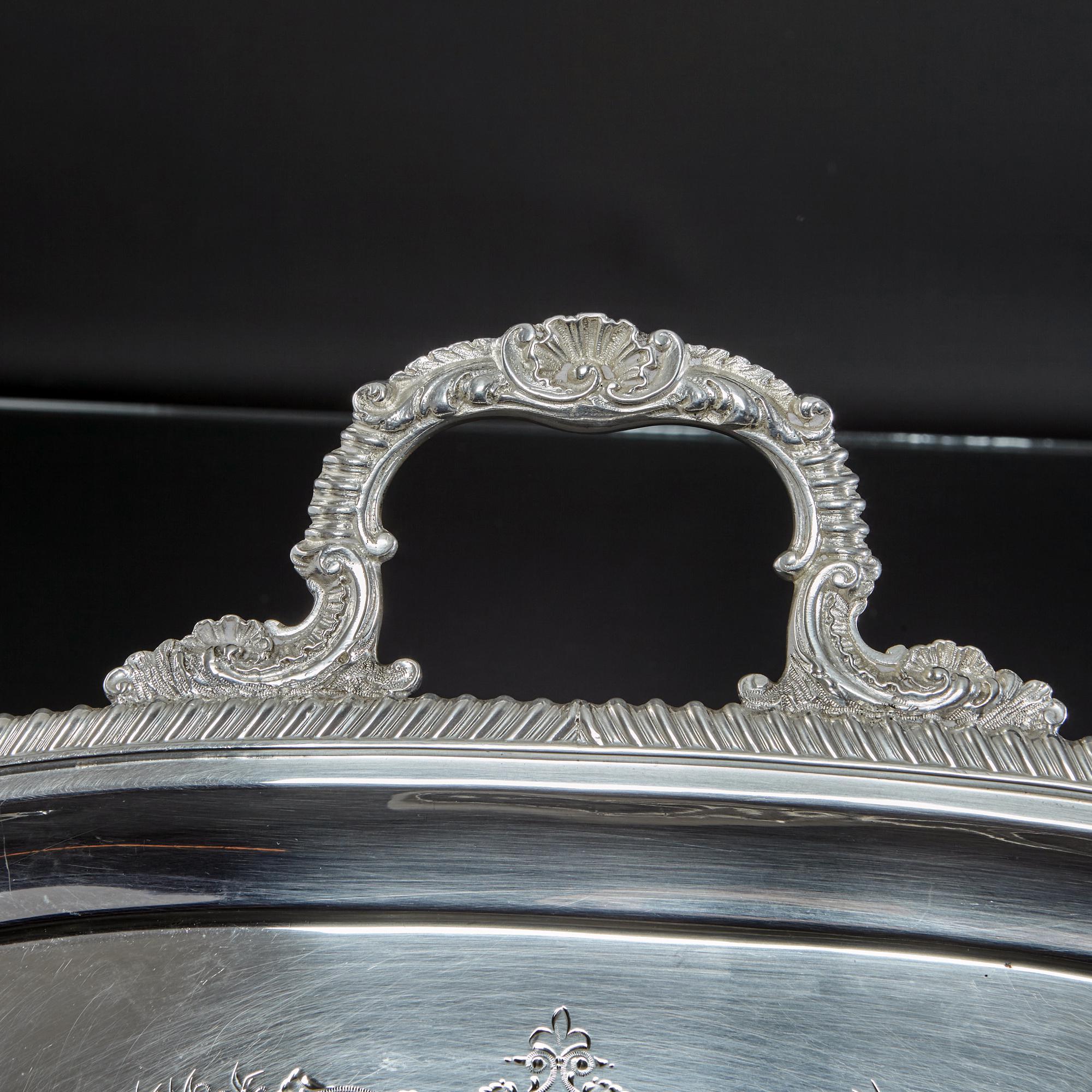 This rectangular antique Edwardian silver tray is impressive, featuring a crisply detailed gadroon border with shell, leaf and scroll corners and side mounts. The handles have similar detailing and the surface of the tray is hand engraved with