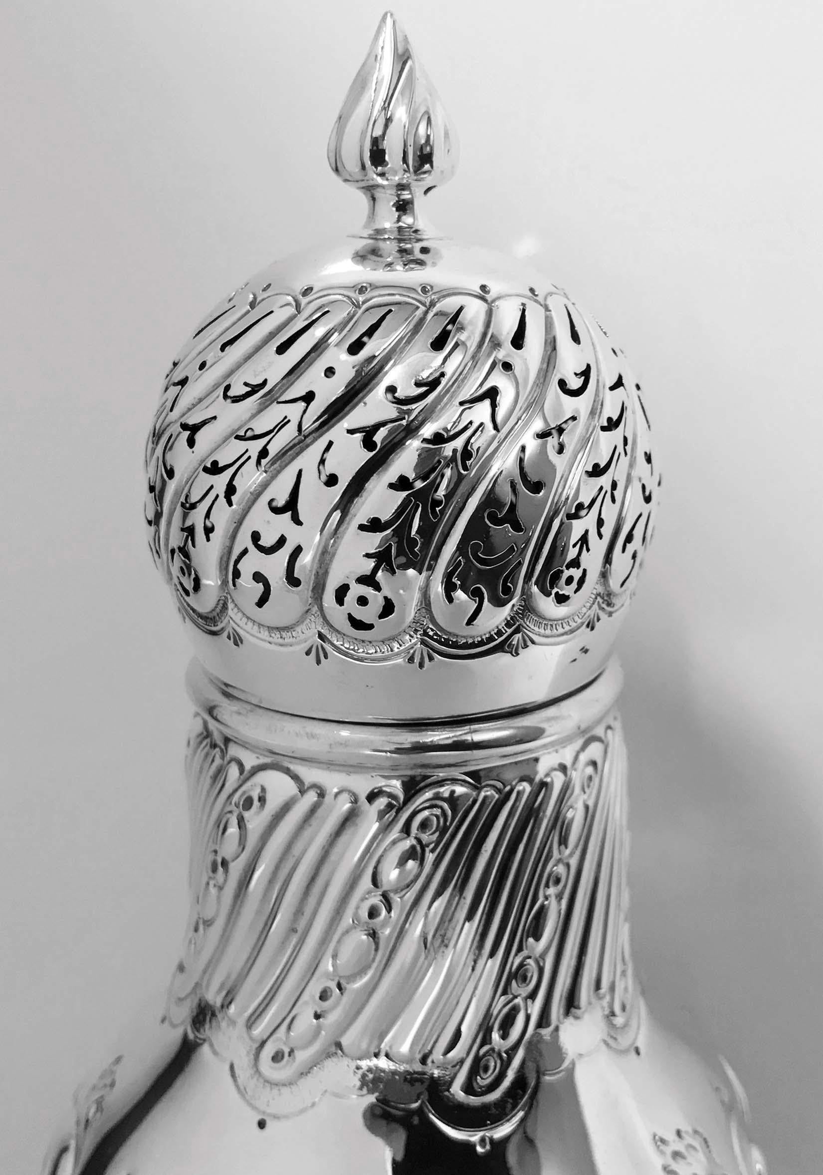 Large antique silver sugar caster, London 1899, William Gibson. The caster on pedestal base rising to tapered baluster body all with lobate swirl embossed design surround, the detachable large bulbous cover, swirl lobate pierced surround with flame